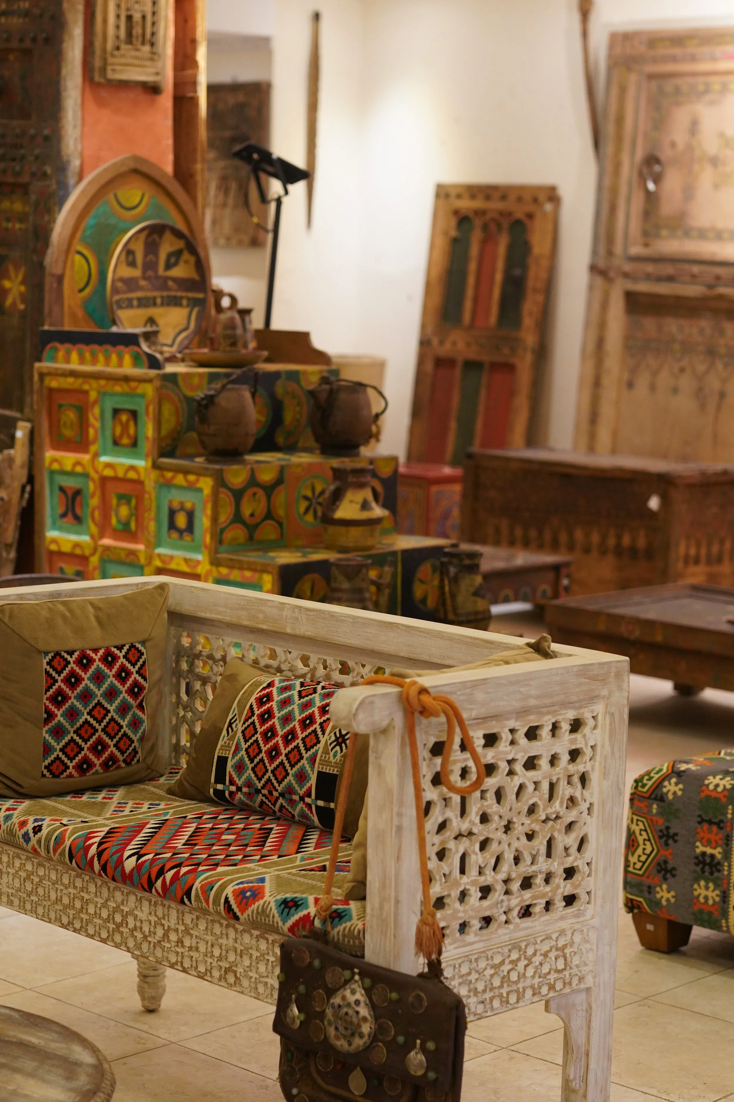 Mobilier de style marocain avec des coussins, un fauteuil en bois peint, et des objets décoratifs en bois et céramique dans une boutique d'artisanat.