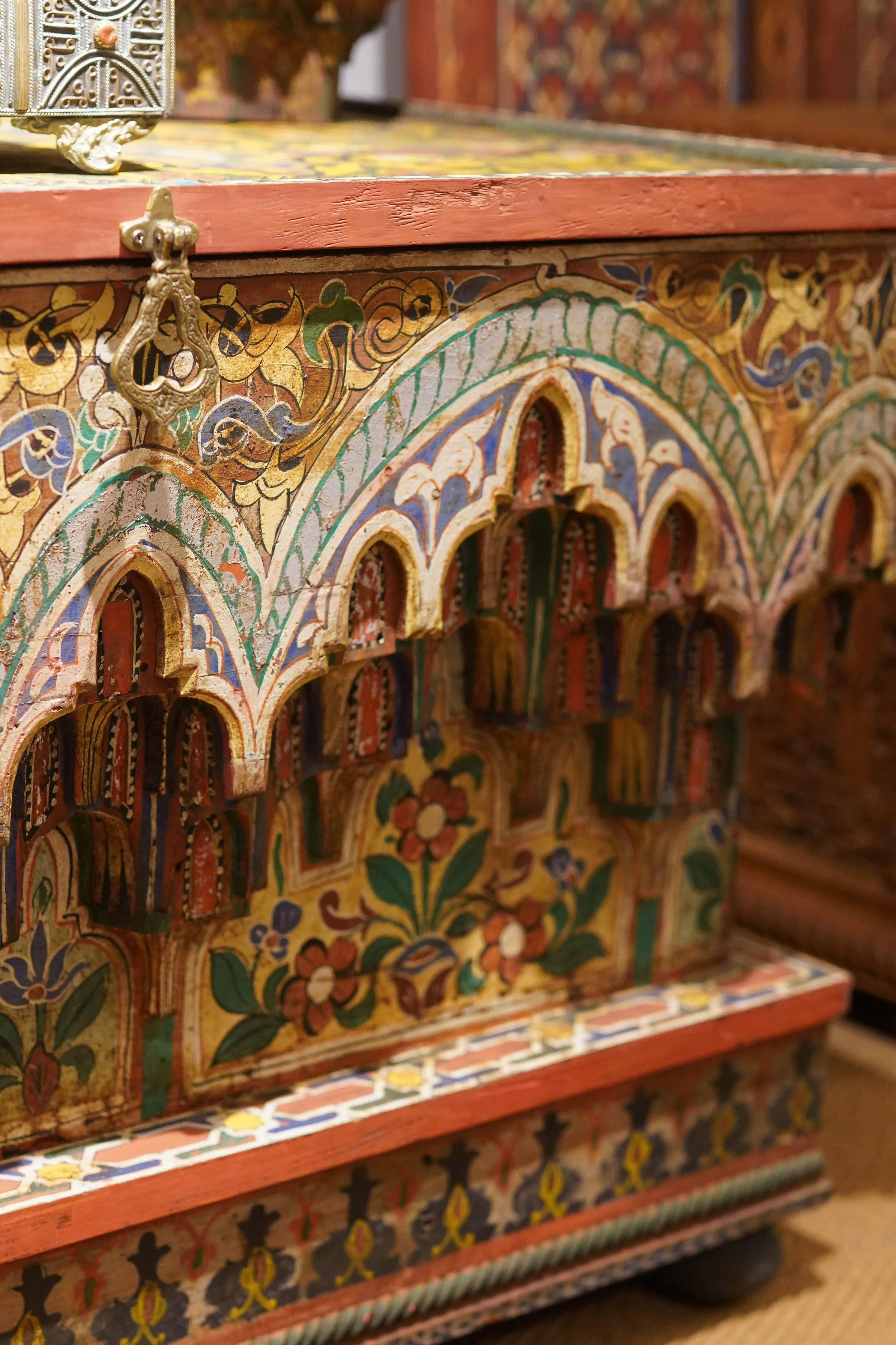 Une boîte en bois décorée de motifs colorés, avec des arches sculptées et une ferrure en métal doré, dans un style artistique traditionnel.