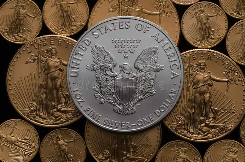 Close-up of various U.S. coins, with a large silver dollar coin in the center showing the eagle emblem, surrounded by smaller copper-colored coins.
