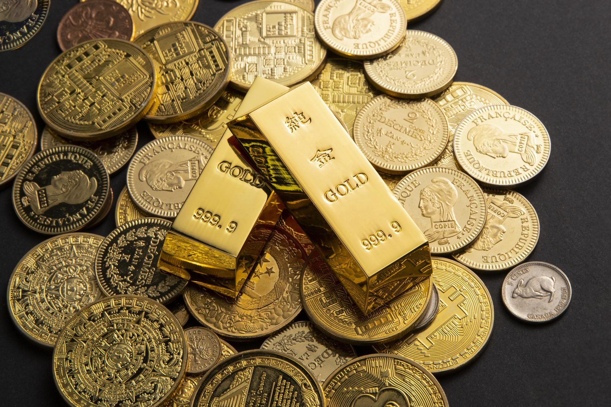 Gold bars and coins, including U.S. quarters and a one-franc coin, arranged on a dark surface.