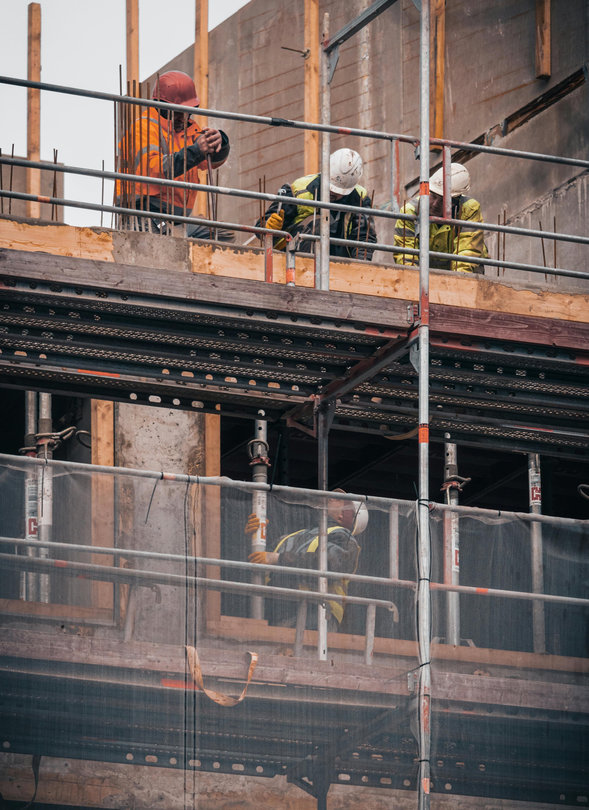 Construction workers wearing safety gear, including helmets and vests, working on a building at a construction site with scaffolding.