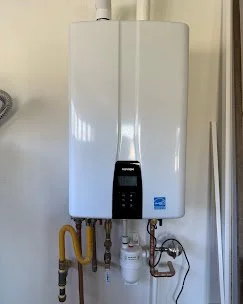 Wall-mounted white tankless water heater with digital control panel and connected piping. Plumbing, HVAC, and mechanical outline icon for A&K Plumbing and Mechanical.