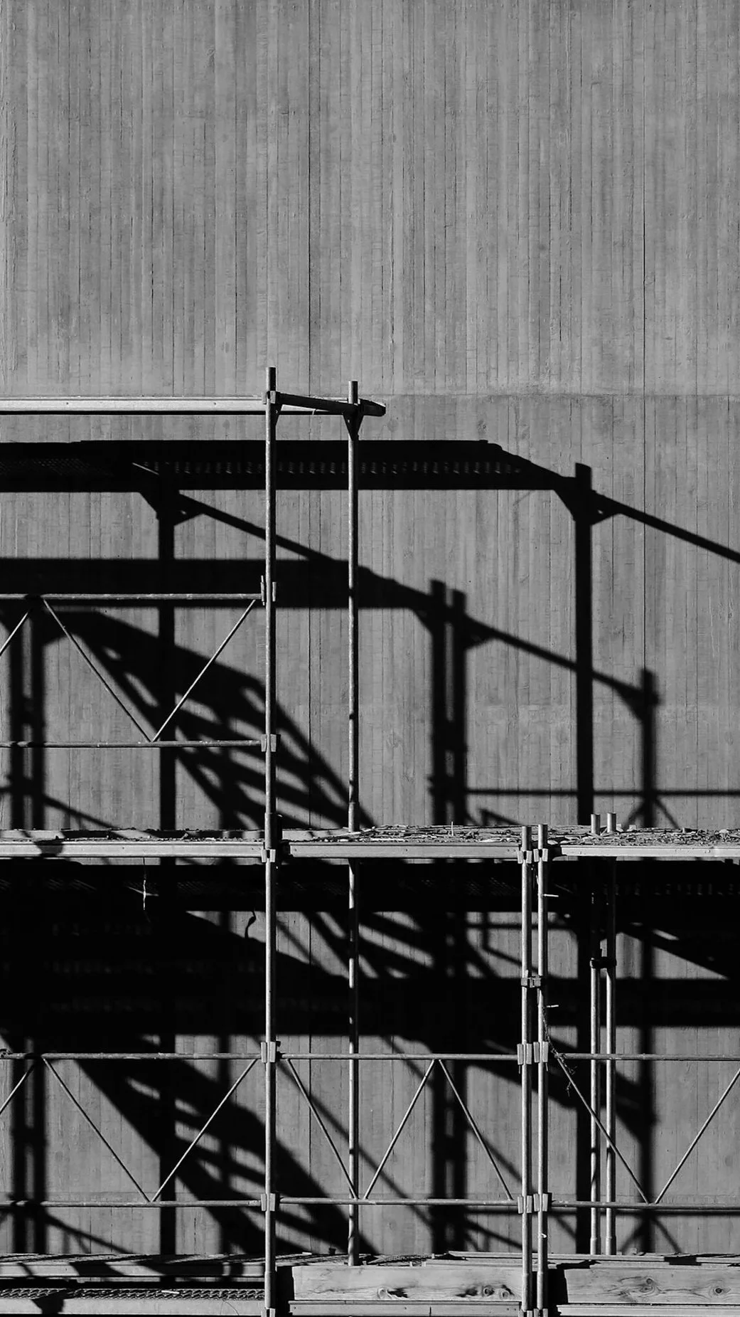 Black and white photograph of scaffolding against a concrete wall, with shadows cast by the scaffolding.