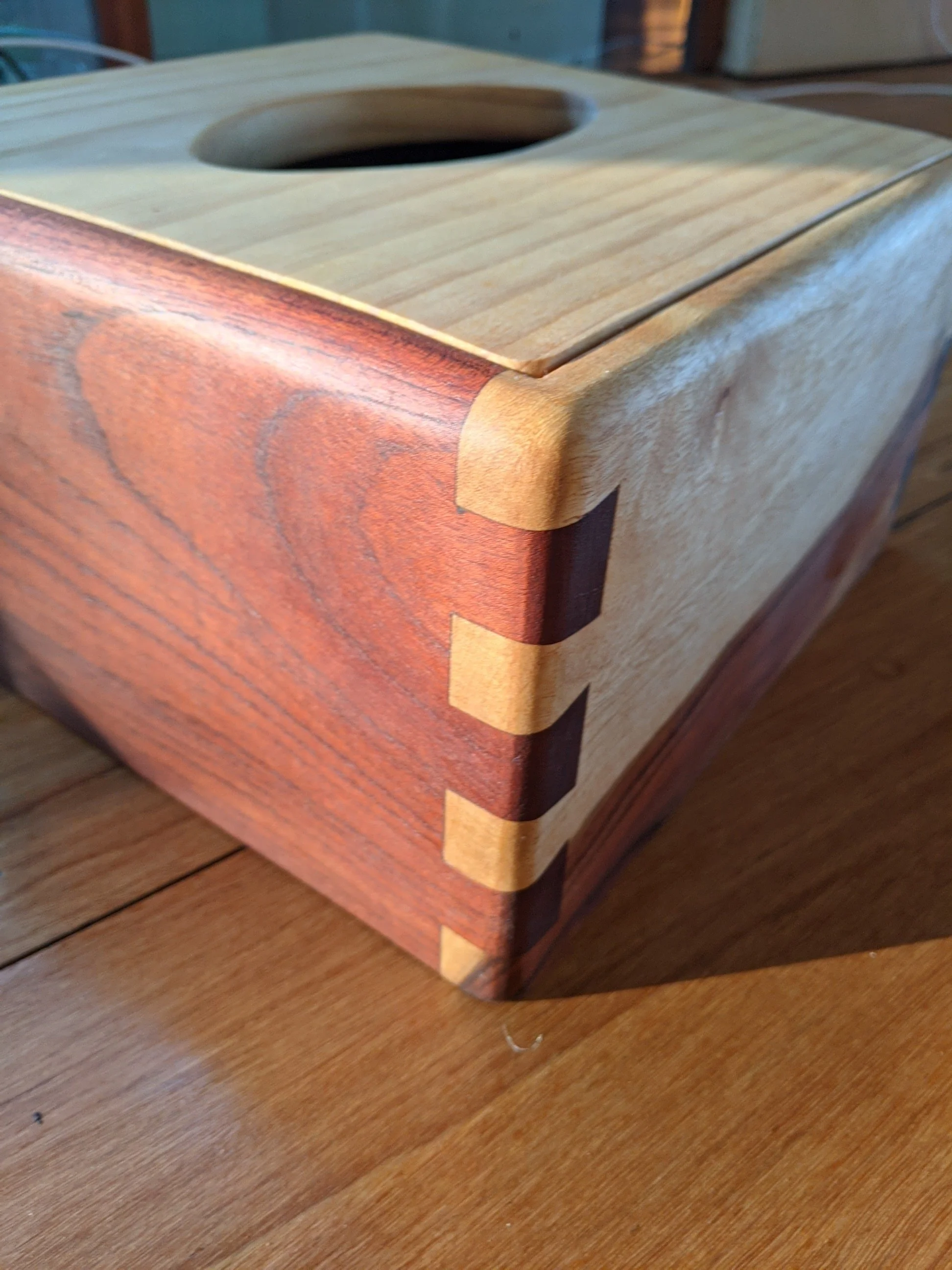 Close-up image of a wooden box with dovetail joints, sitting on a wooden surface.