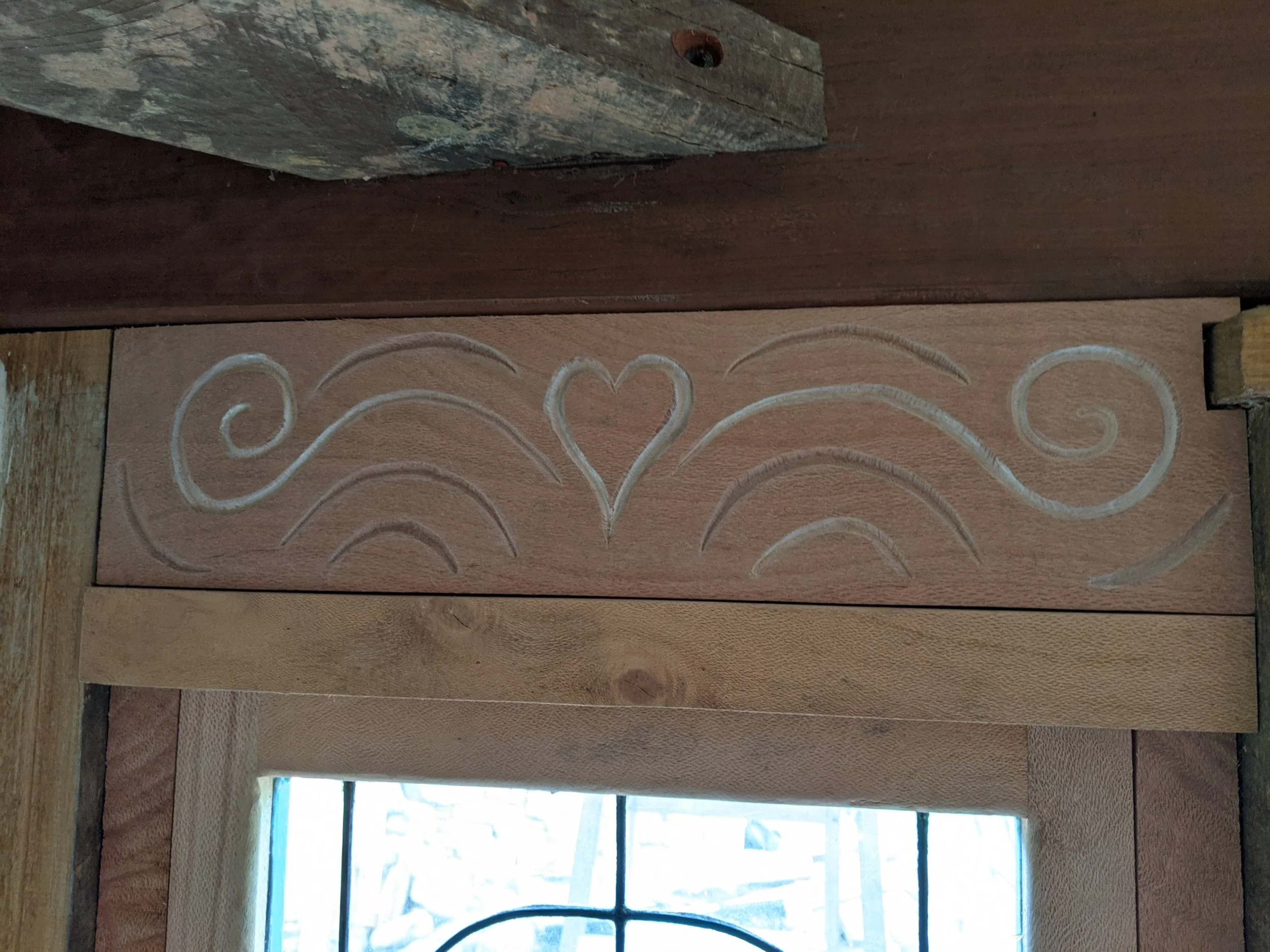 Wooden deck floor with decorative white swirl pattern and exposed framing, view through a window with sunlight.