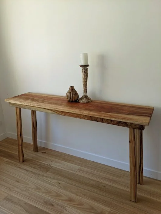 A wooden console table against a white wall with a decorative candle holder and a small wooden vase on top.