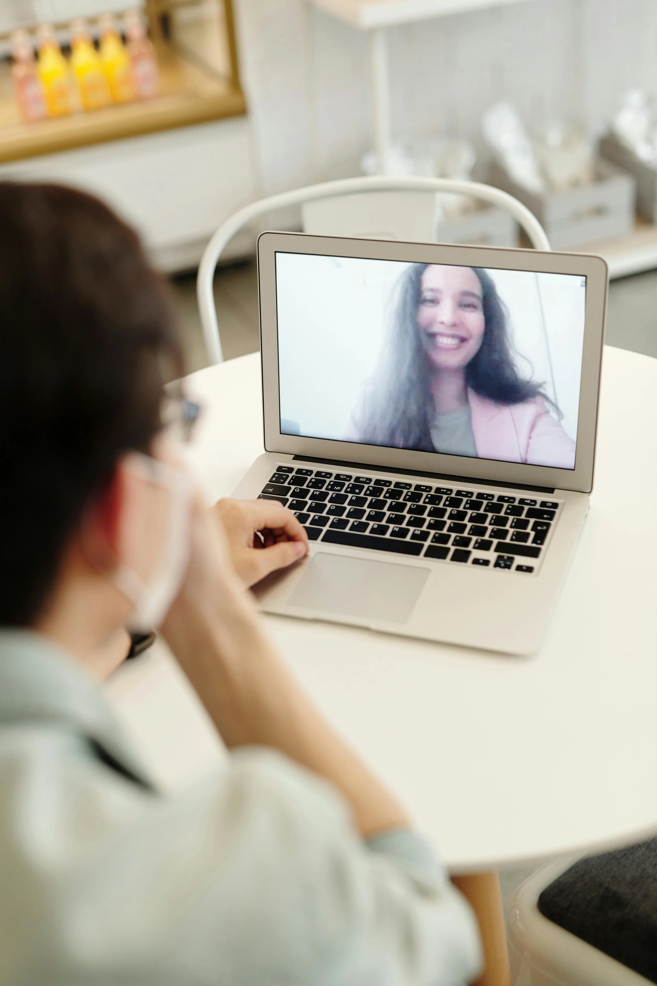 A person sitting at a desk on a video call with a woman displayed on a laptop screen, smiling.