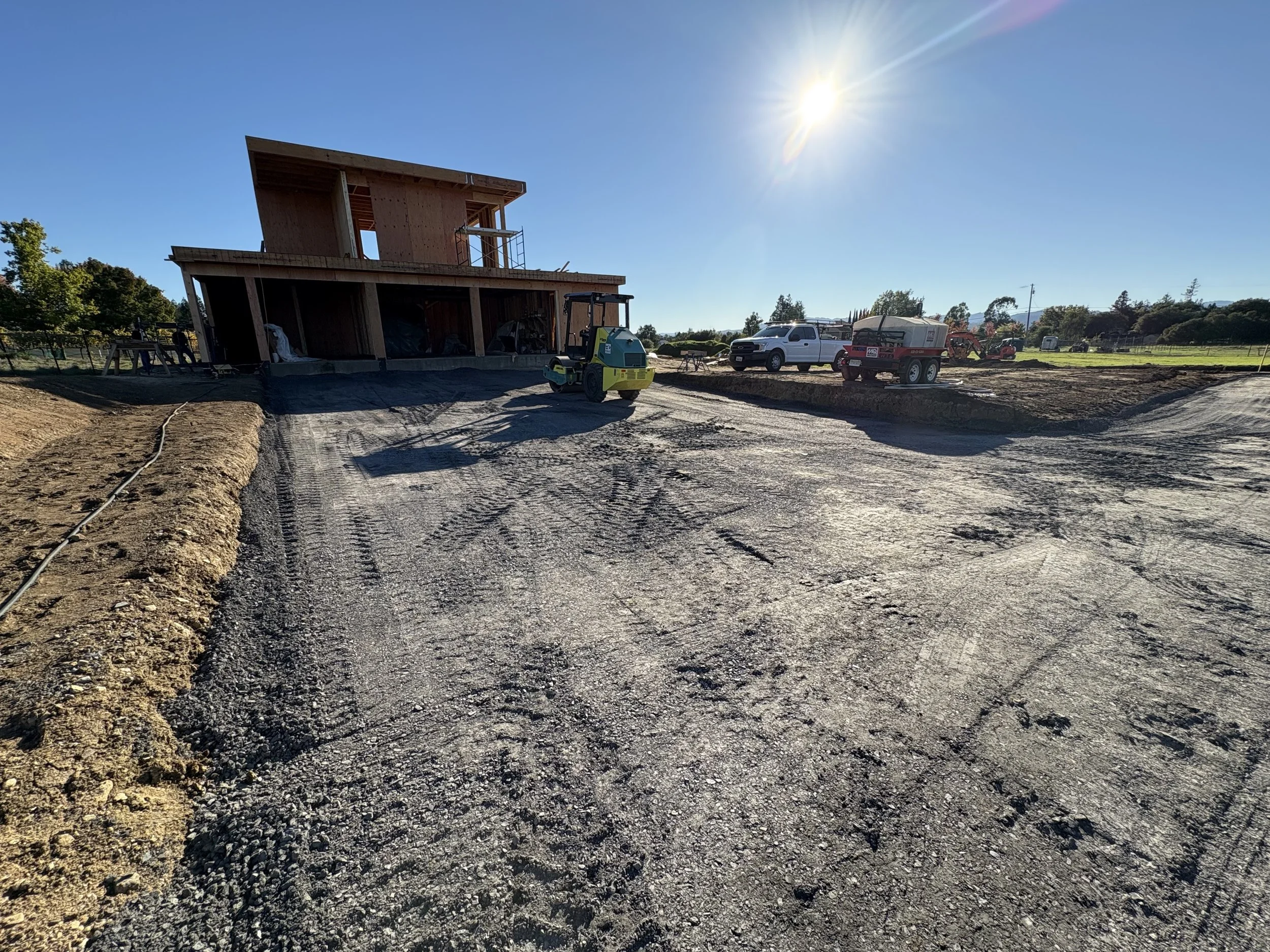 Construction site with a building under construction, construction vehicles, and equipment, with a clear blue sky and bright sunlight.