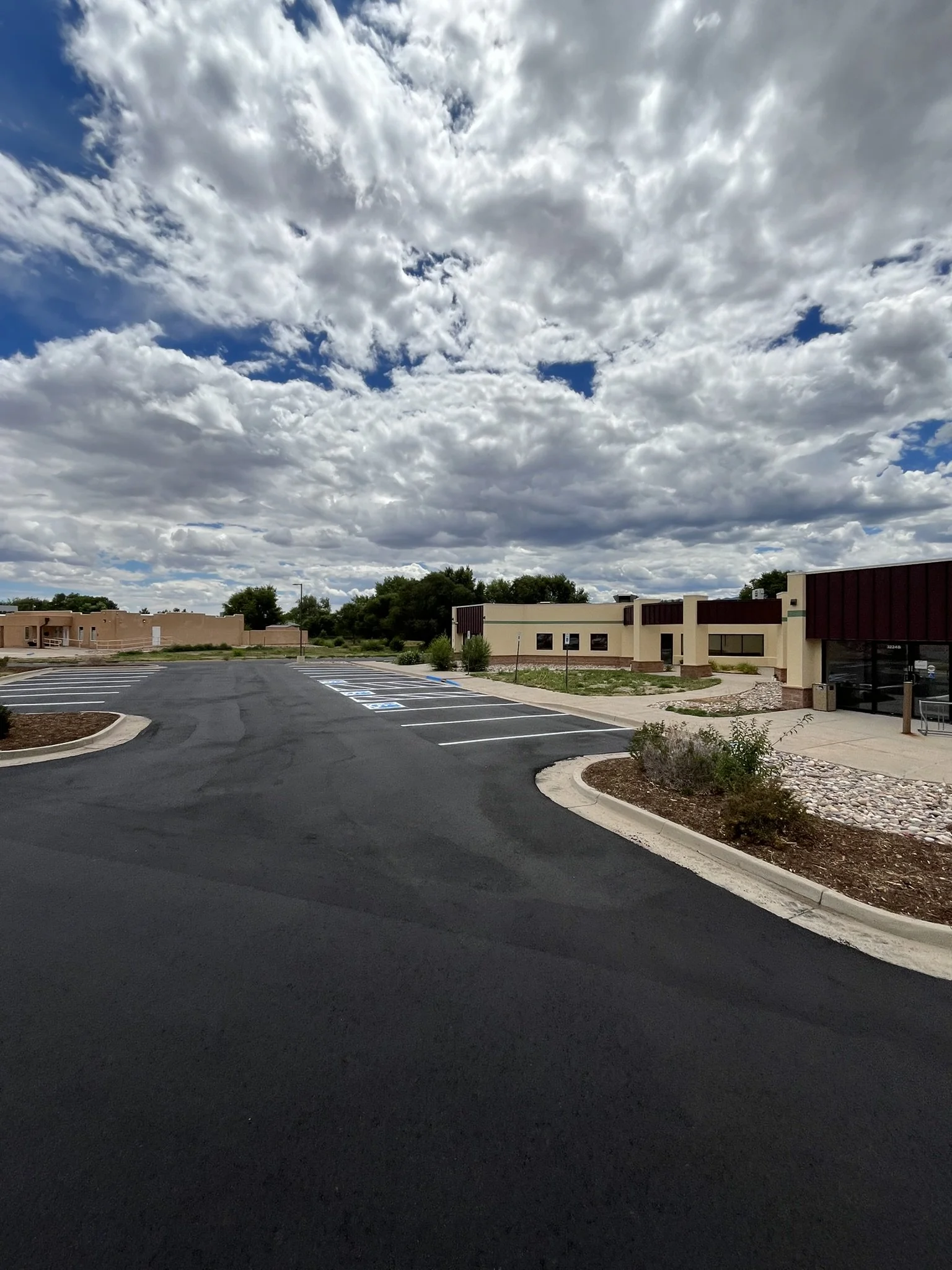 Empty parking lot with marked spaces and a small building under cloudy sky.