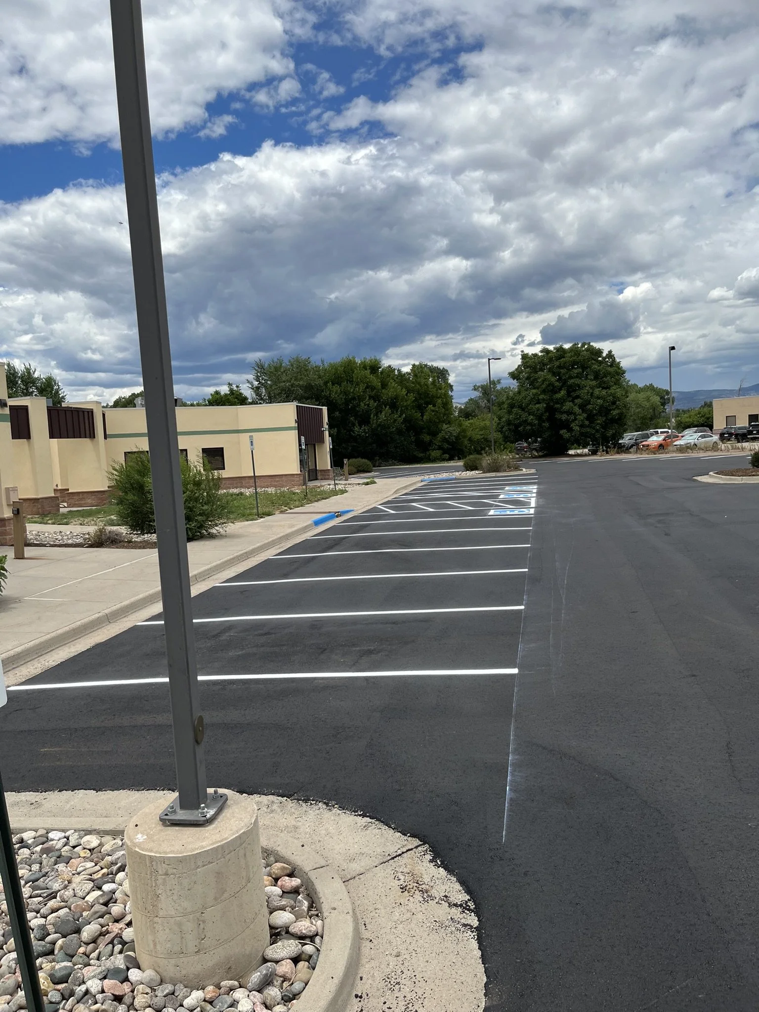 Empty parking lot outside a commercial building with trees and cloudy sky.
