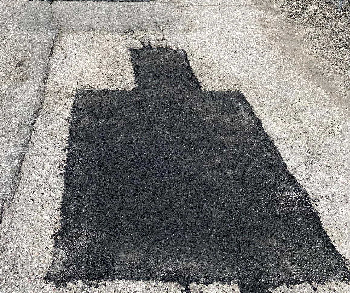 Freshly patched pothole on a paved road with asphalt.