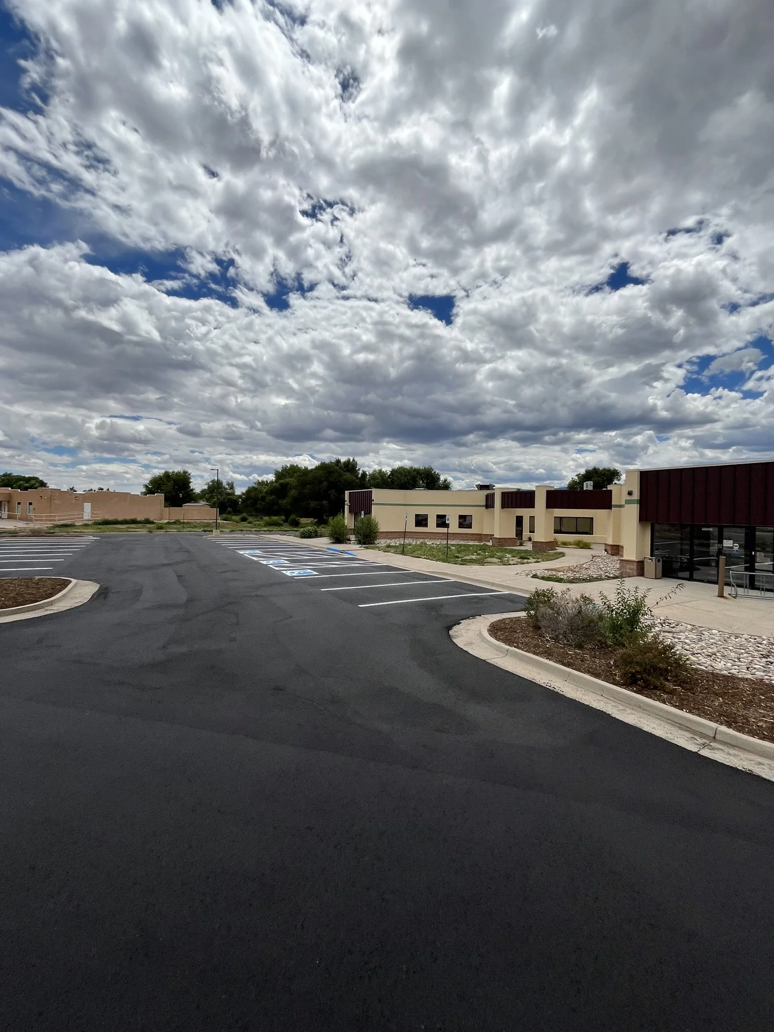 Empty parking lot in front of commercial buildings on a partly cloudy day.