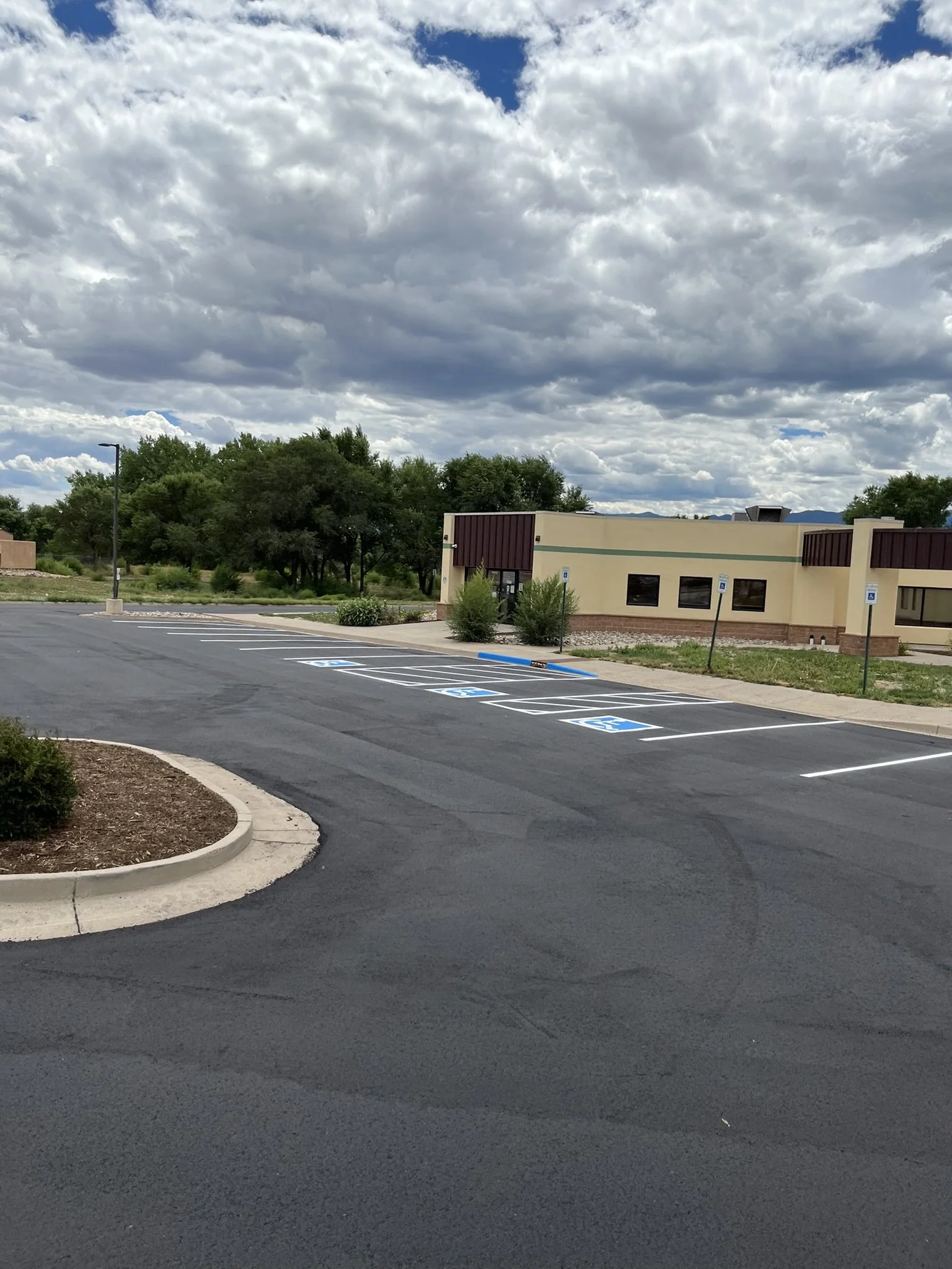 Empty parking lot with marked handicapped parking spaces and a beige building with trees and cloudy sky in the background.