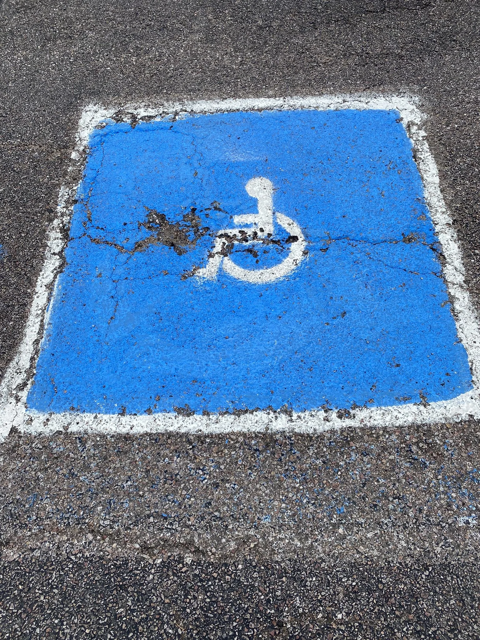 A parking space with a blue and white wheelchair accessible symbol painted on the asphalt ground.