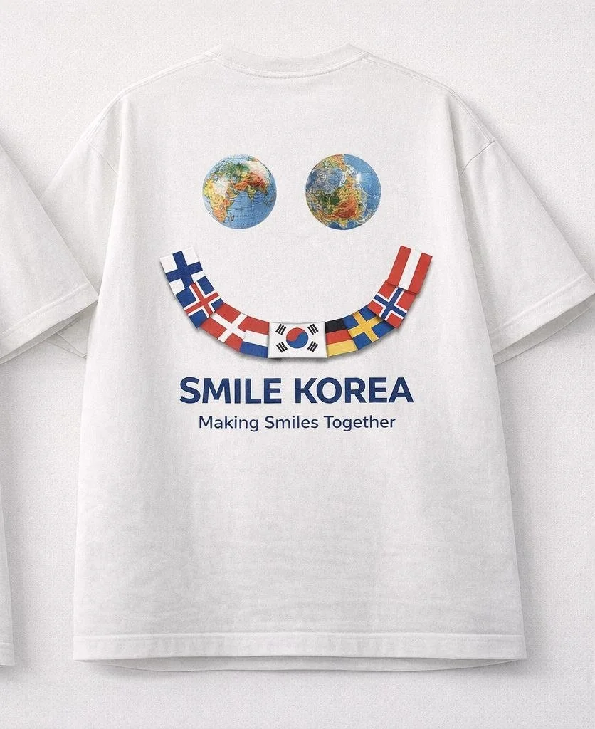A white T-shirt features a smiley face made up of two images of the globe as eyes and flags of various countries, including Norway, South Korea, Sweden, and others, forming the mouth. Below the face, the text reads 'SMILE KOREA' with the tagline 'Making Smiles Together'.