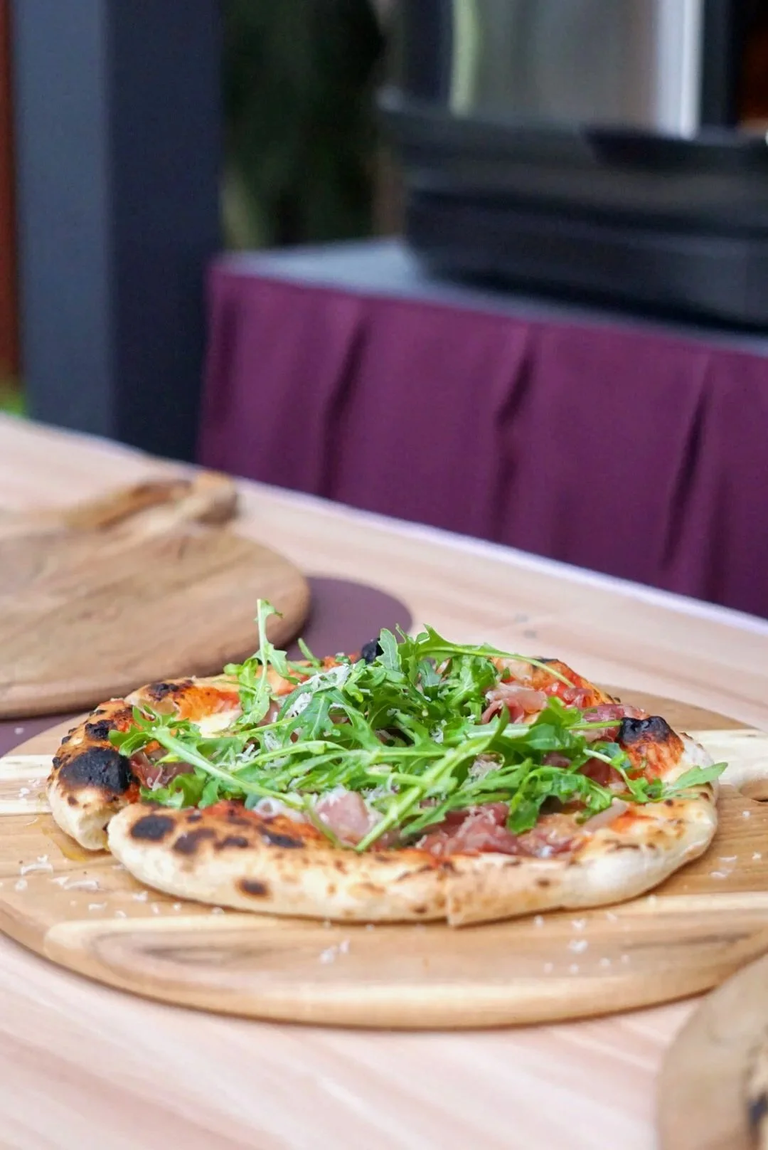 Fresh pizza topped with arugula on a wooden serving board.