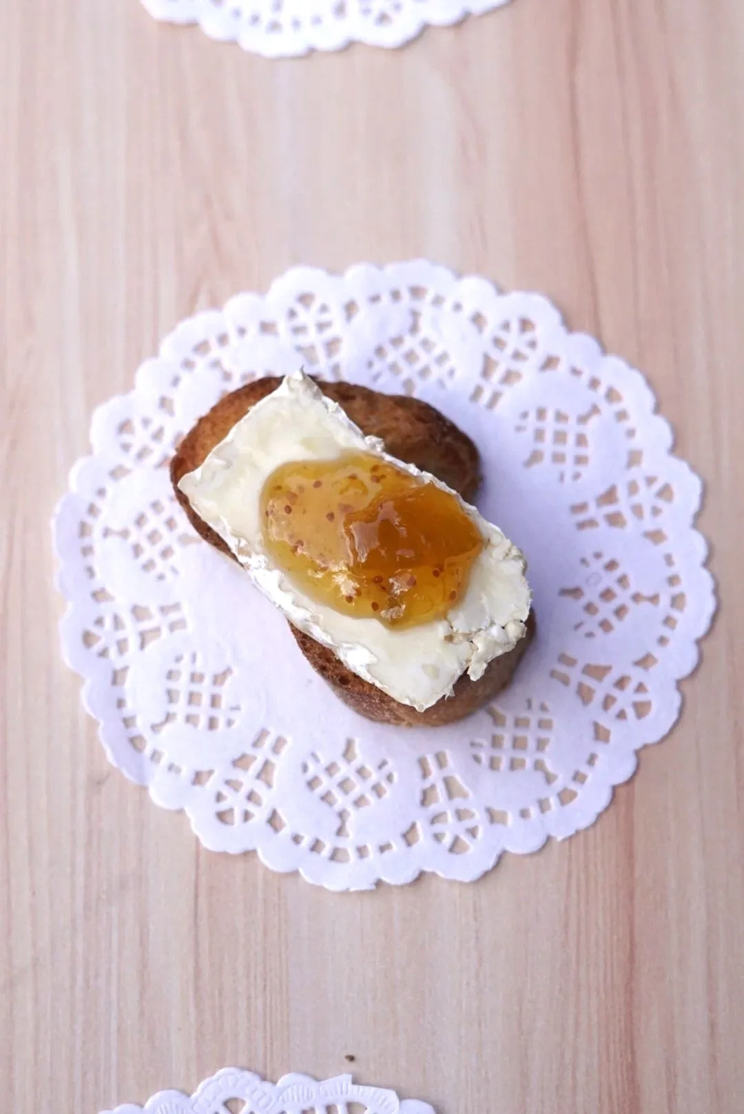 A piece ofbread with cheese on top, placed on a white paper doily on a light wooden surface.