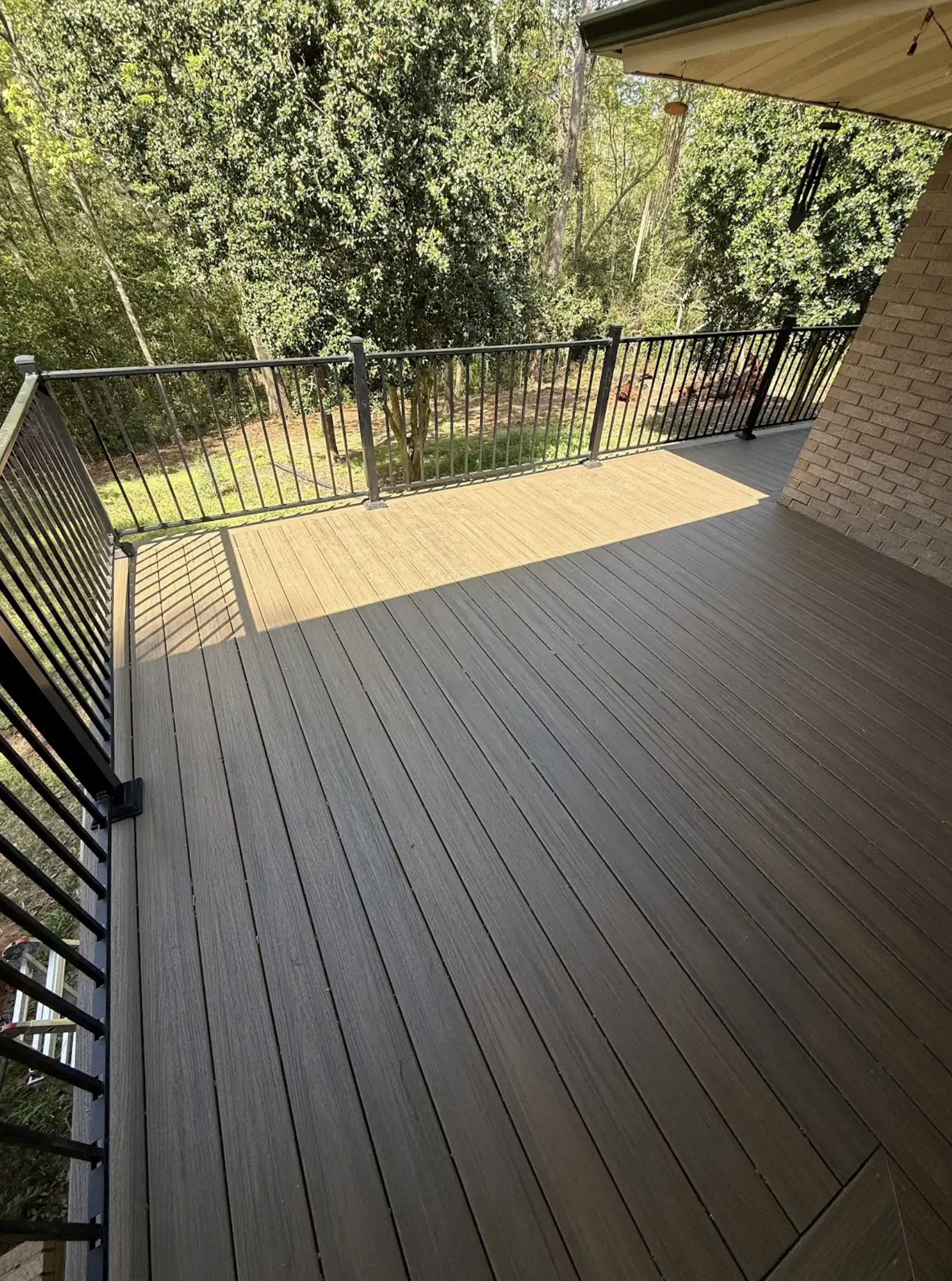 View of a wooden deck with metal railing, partially shaded, overlooking a backyard with grass and trees.
