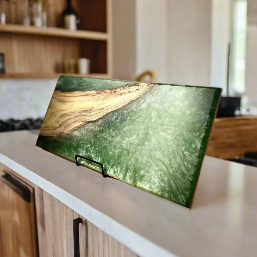 A glass cutting board with a woodland scene of a tree branch and green forest leaves, displayed on a kitchen countertop.