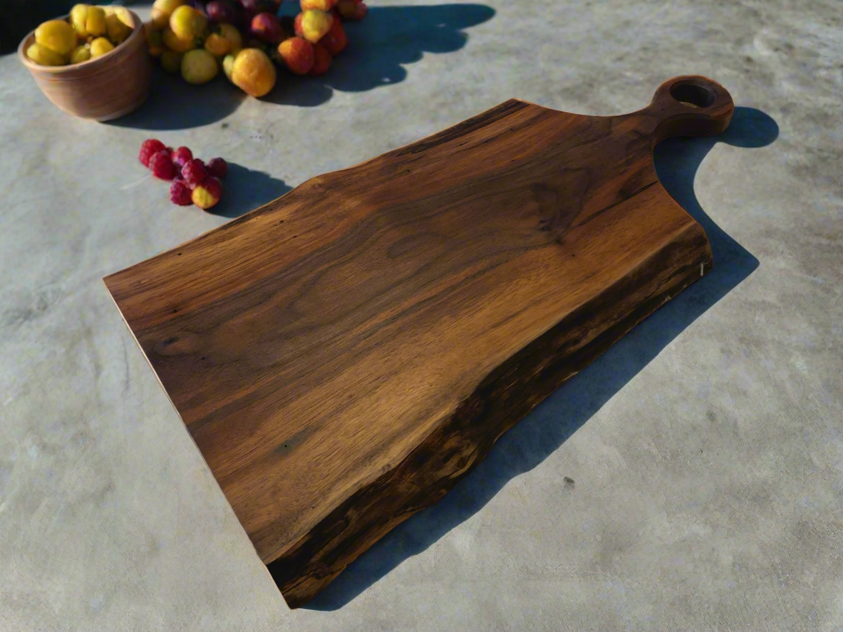 A wooden serving board with a handle, placed on a light surface with a small bowl of yellow fruit and a cluster of small red and yellow berries nearby.
