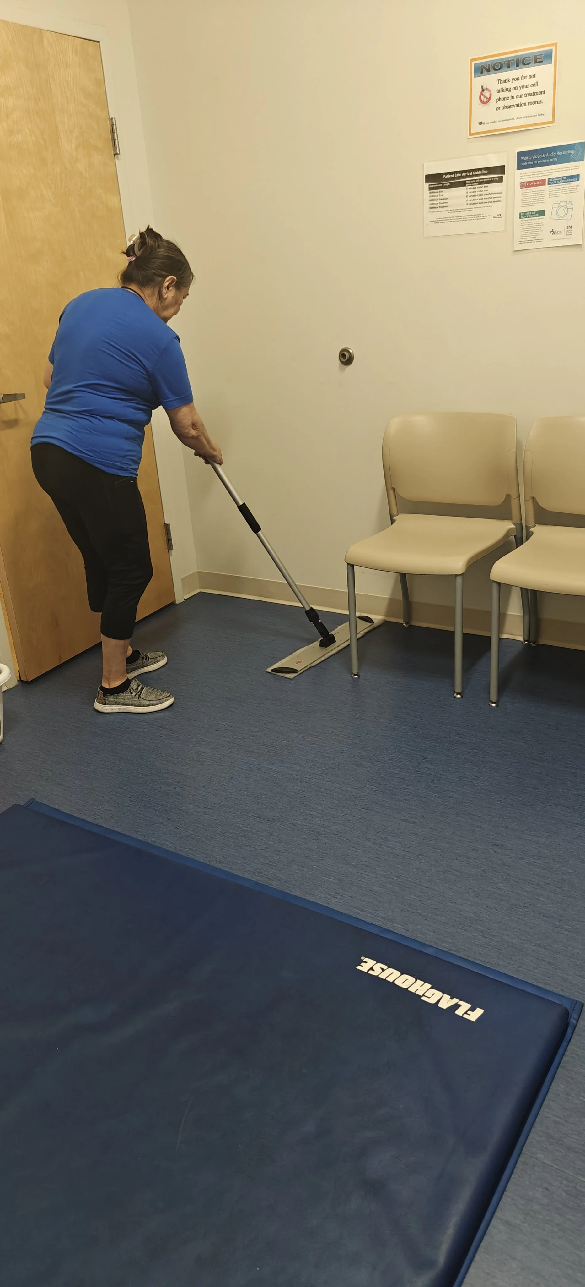 Mujer limpiando el suelo en una sala de espera con sillas y un tapete de yoga.