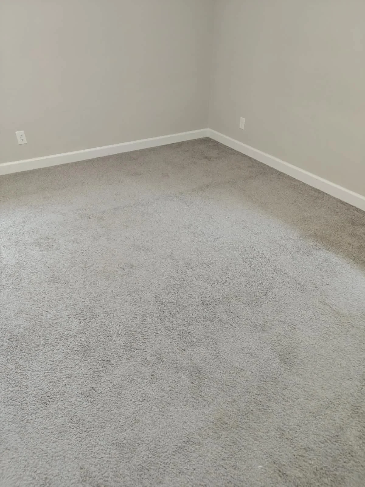 Habitación vacía con paredes blancas y alfombra gris.