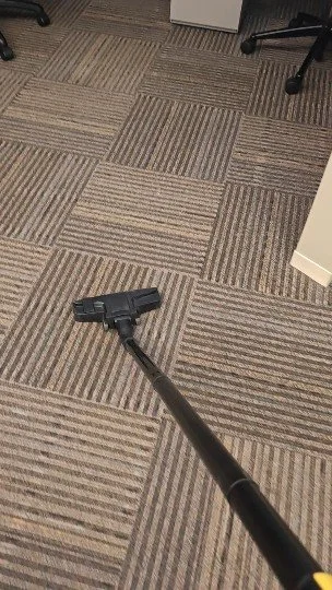 Aspiradora en el suelo de una oficina con alfombra de patrón de cuadros.