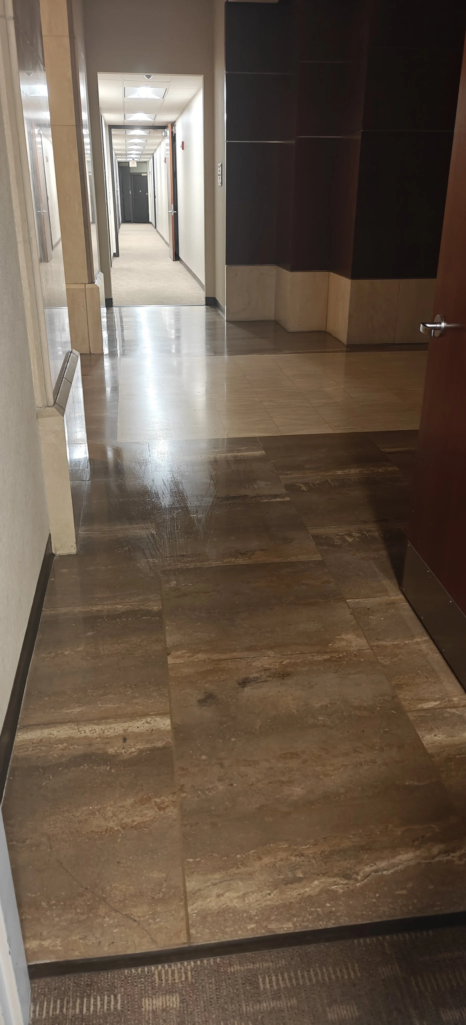 Pasillo en un edificio de oficinas con paredes claras, puertas cerradas y un suelo de baldosas de colores marrones y beige.