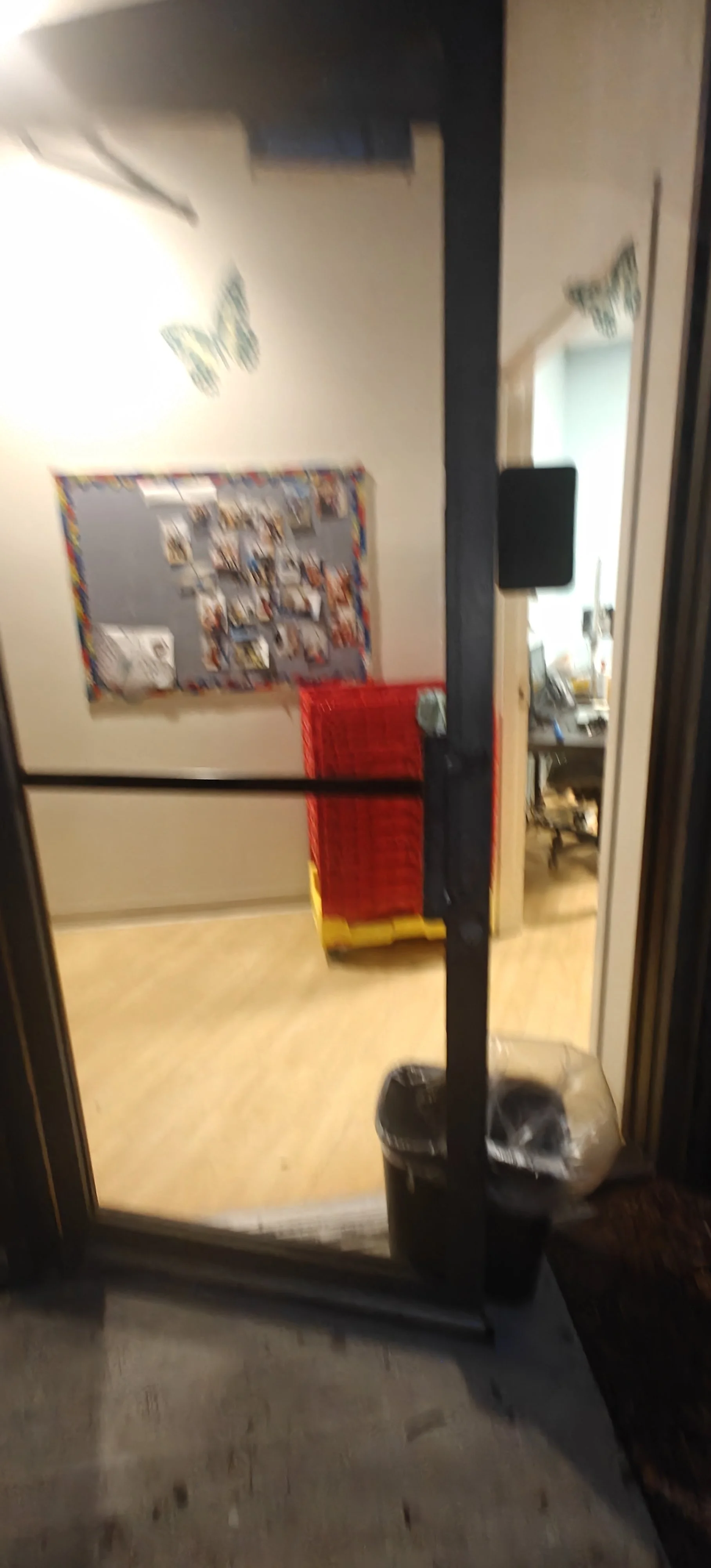 Vista desde afuera de un pasillo que da a una oficina o aula con una pizarra en la pared y una mesa con computadora y sillas. Frente a la entrada, hay un bulto con una bolsa de plástico.