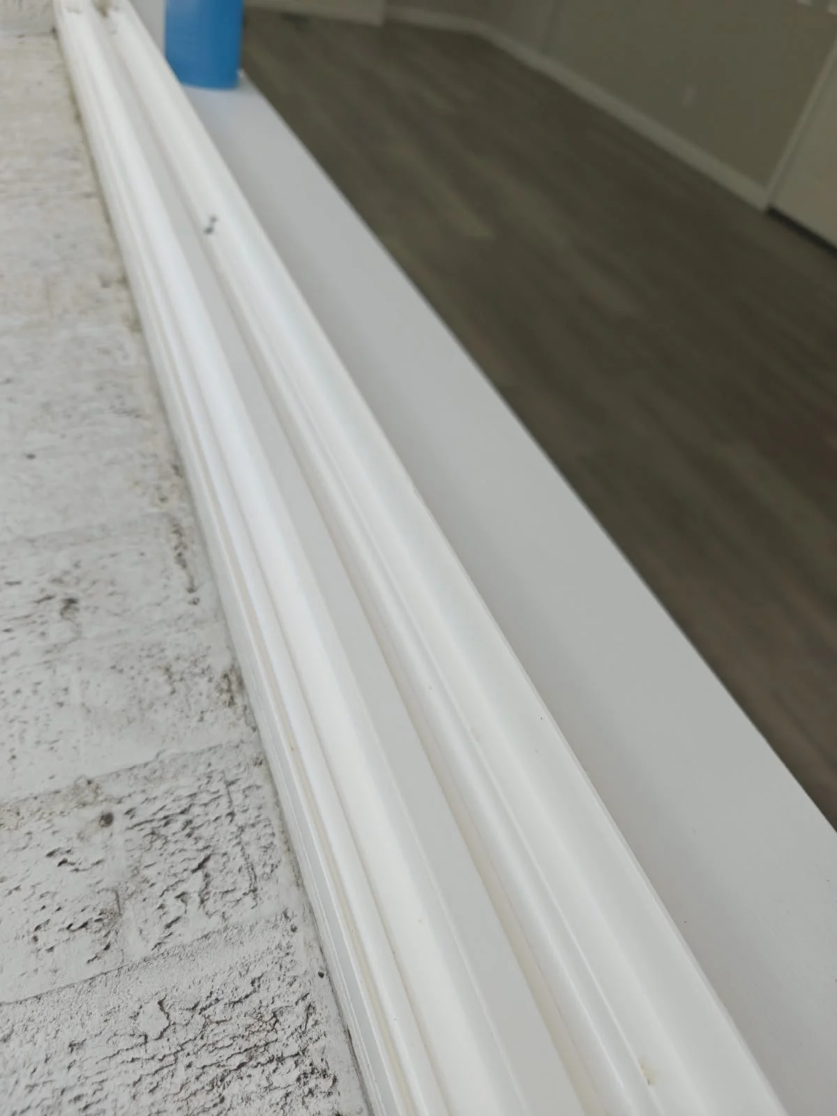 Línea de moldura blanca en el pasillo, vista desde el piso, con suelo de baldosas y pared de madera en el fondo.