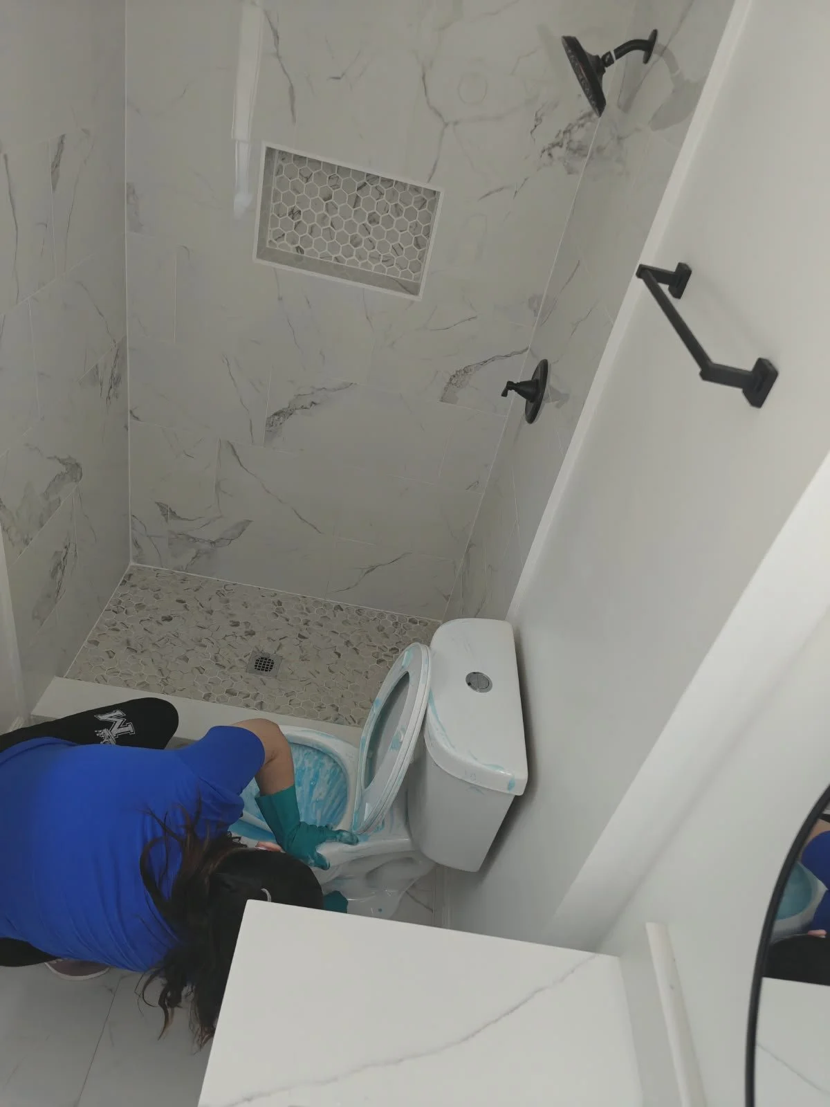 Una persona arrodillada en el baño, lavándose con agua en una taza y con el inodoro abierto.