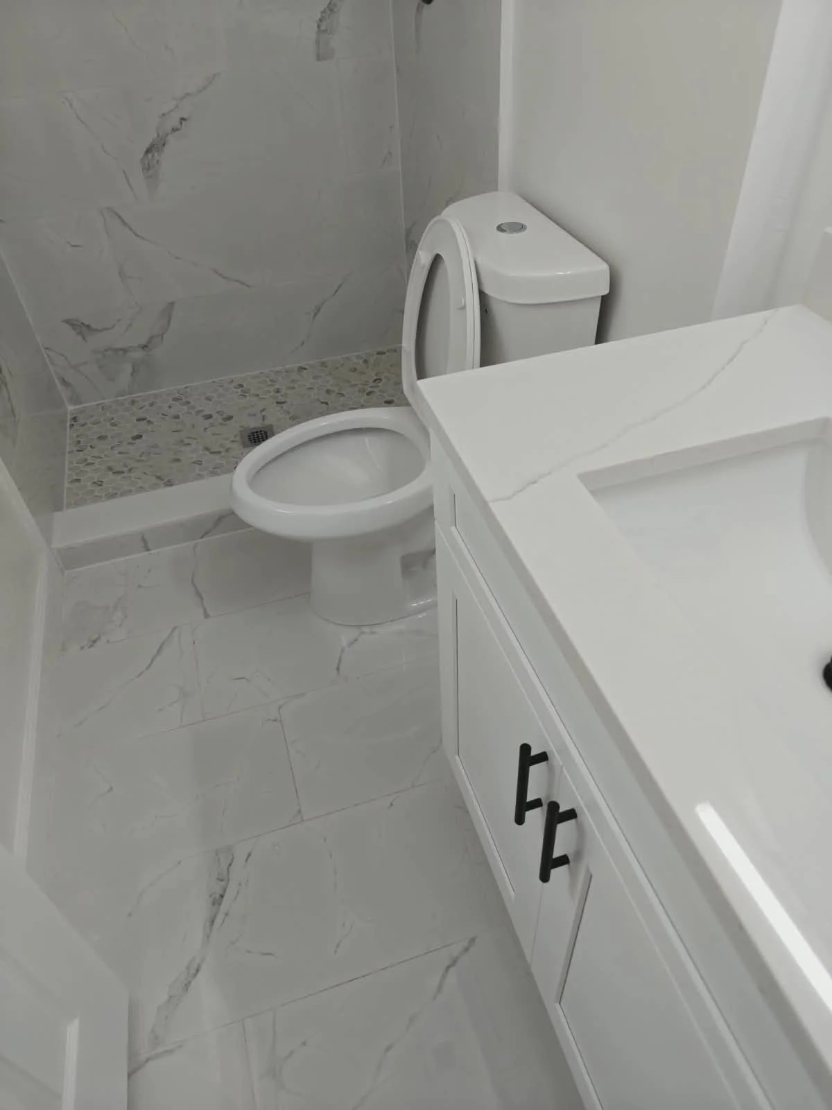 Baño con lavabo blanco, inodoro y ducha con paredes de mármol claro y suelo de baldosas de mármol.