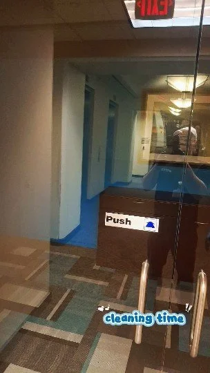 Puerta con señal de 'Push' y cartel que dice 'cleaning time', en un pasillo interior con paredes blancas y piso de baldosas multicolores.