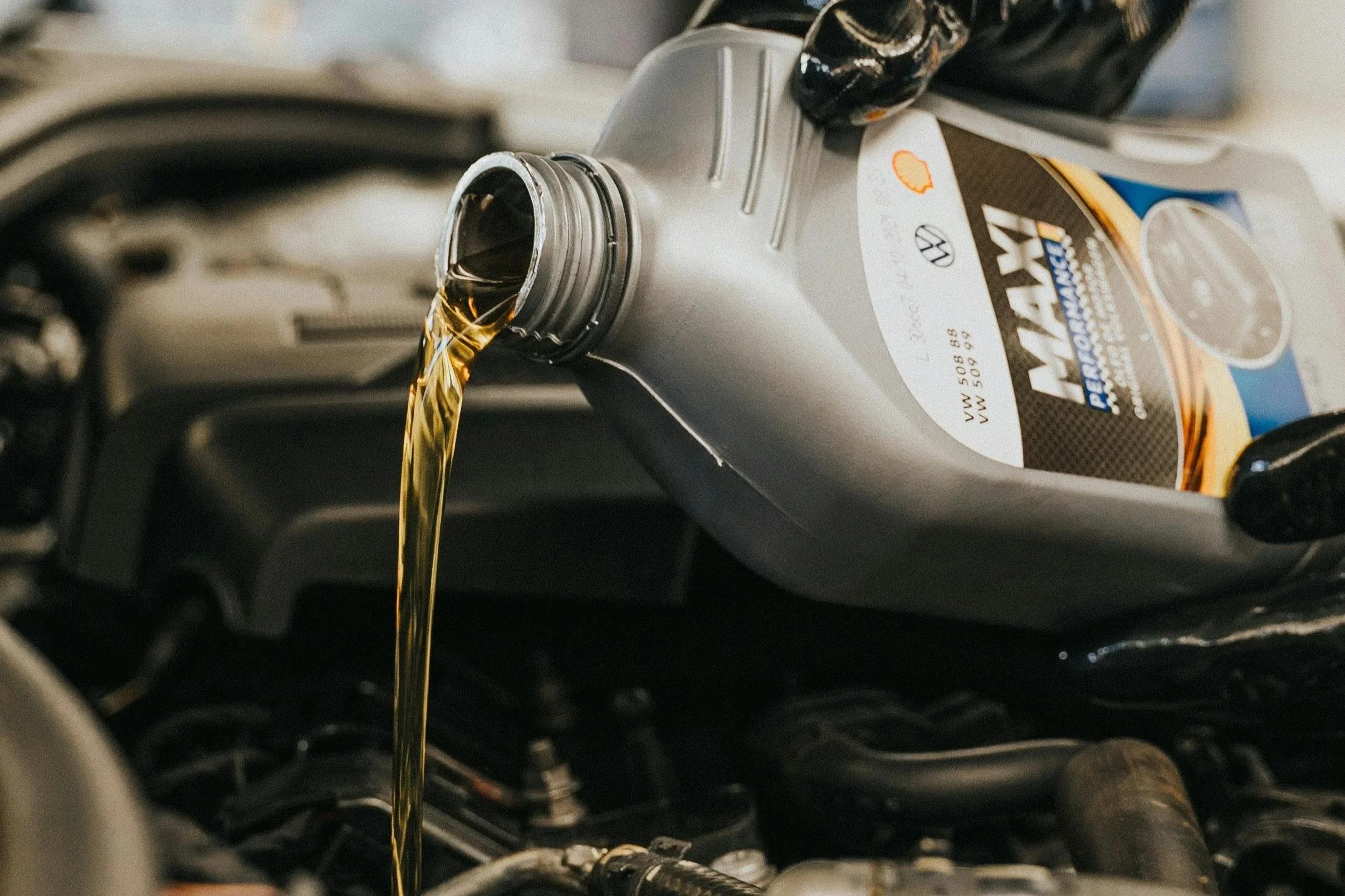 Car engine oil being poured from a container into a vehicle's engine.