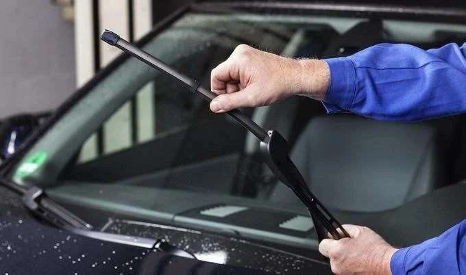 A person in a blue shirt using a windshield ice scraper on a black car with ice or snow on its surface.