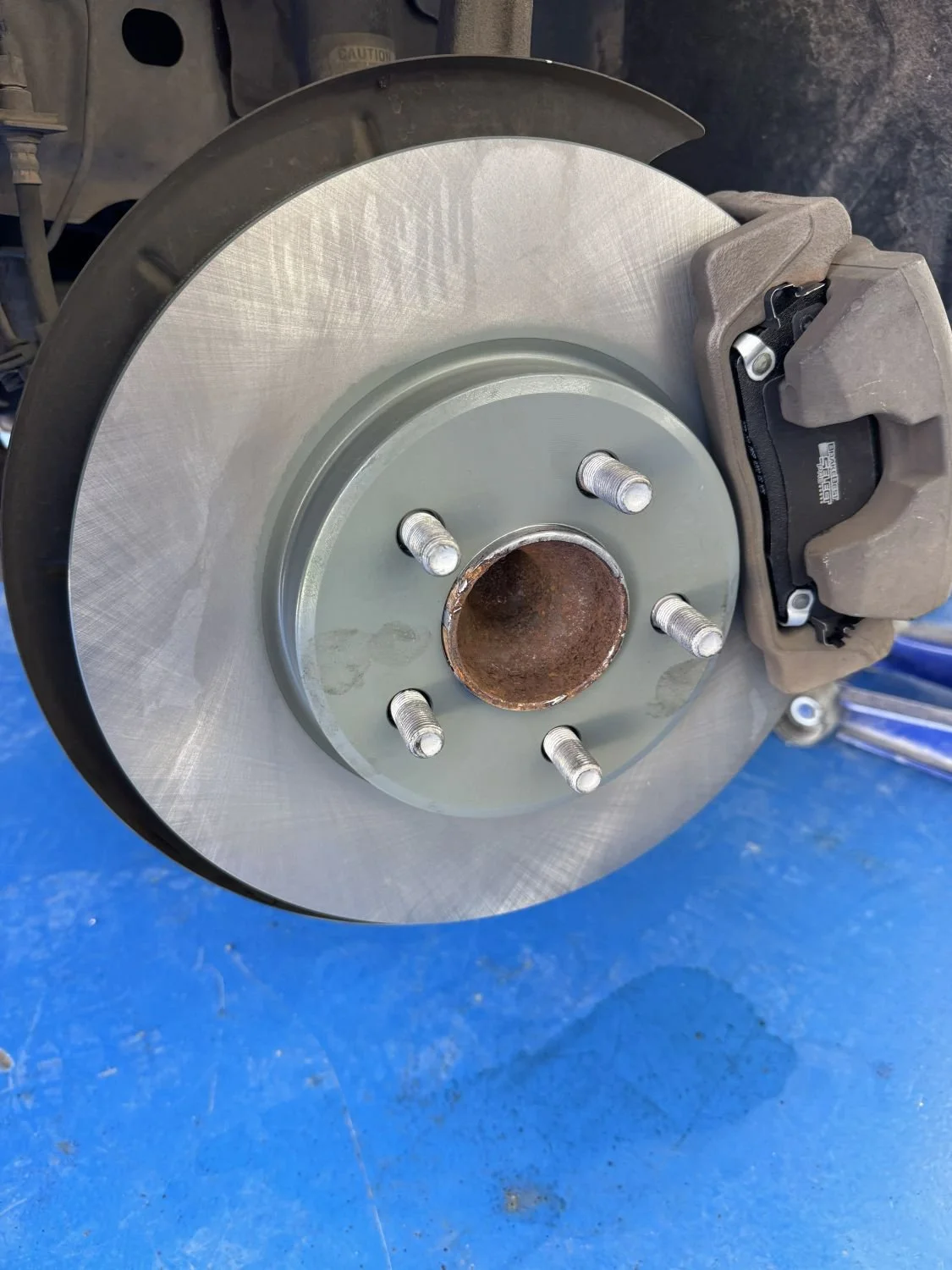 A car brake rotor with a mounted brake caliper, seen from the front on a blue surface.