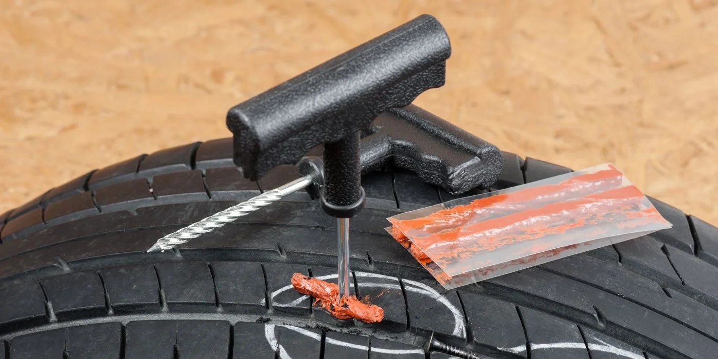 A tire repair kit with a T-handle reamer, a screw, and a piece of rubber strip on a car tire.