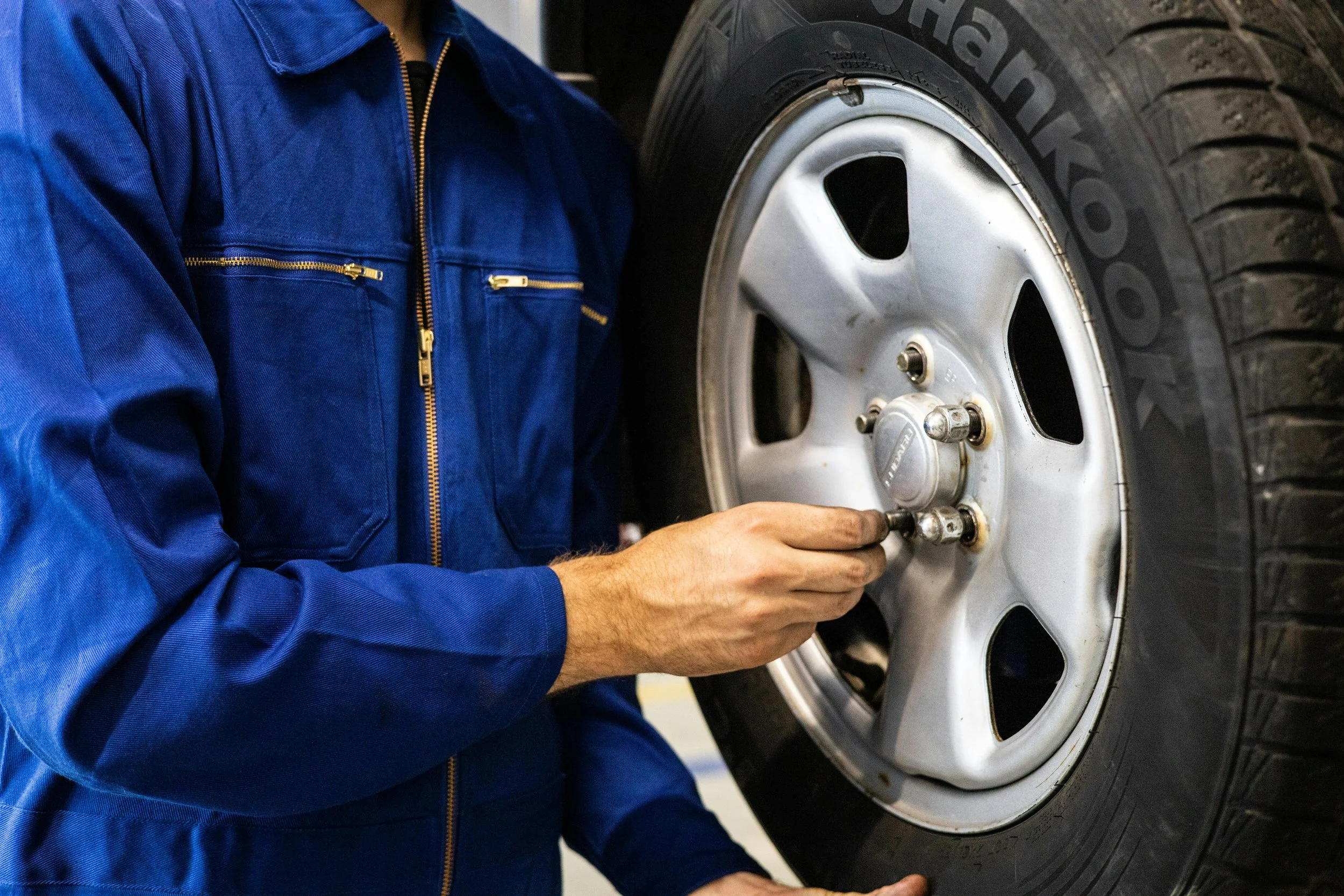 A person in a blue jacket working on a silver car wheel, adjusting the lug nuts.