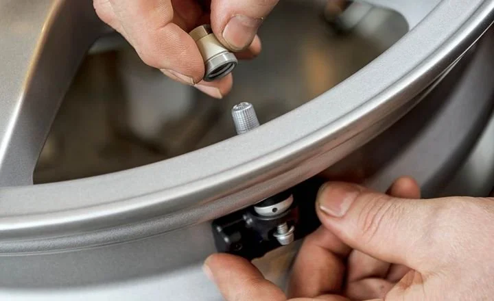 Two hands assembling or repairing a component of a metal or plastic object, possibly involving a small lens or glass part.