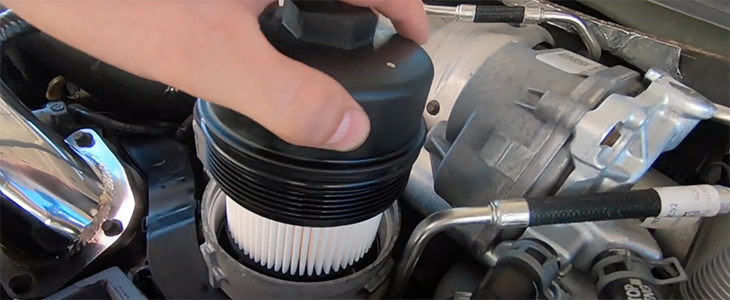 A person's hand inserting a round, pleated filter into an engine compartment.