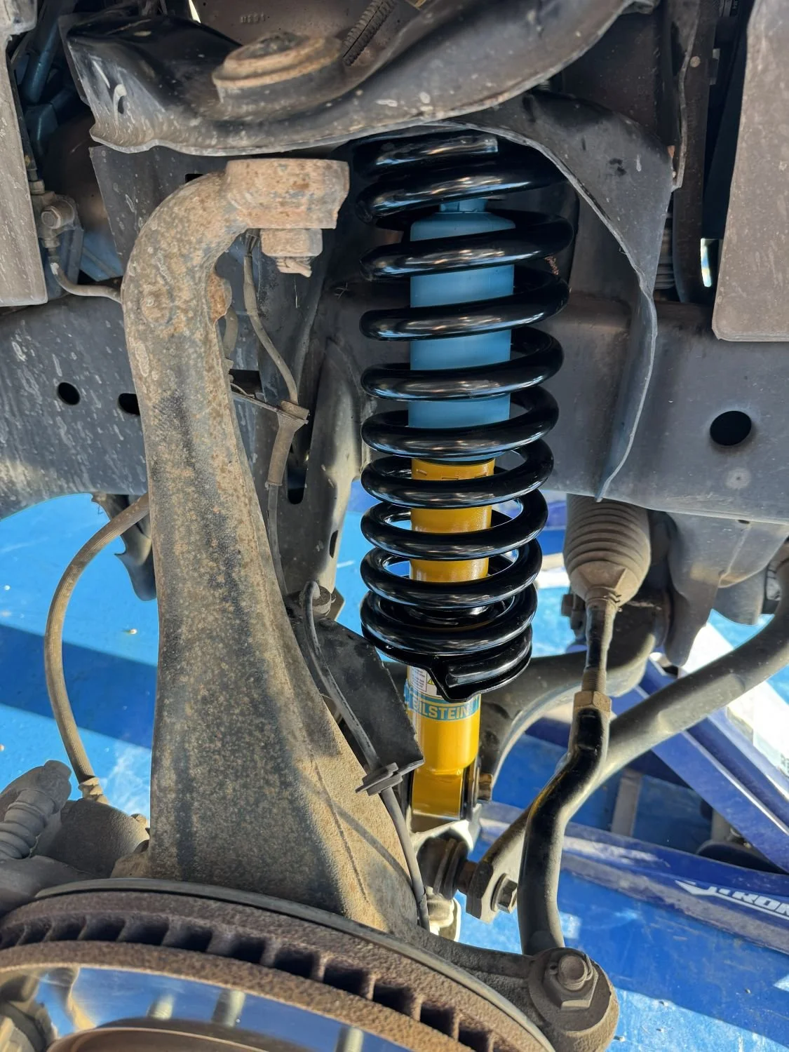 Close-up of a vehicle's suspension system showing a coil spring, shock absorber, and other suspension components.