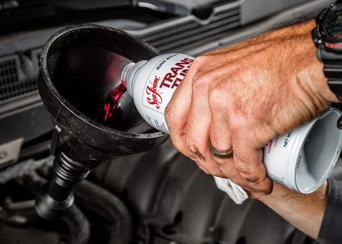 A person pouring Transmission Fluid from a can into a car's transmission fluid reservoir.