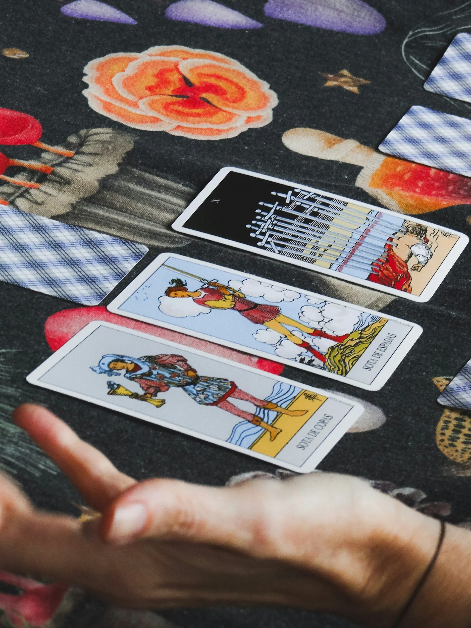 Tarot cards laid out on a table with a floral patterned cloth underneath, with a person's hand in the foreground.