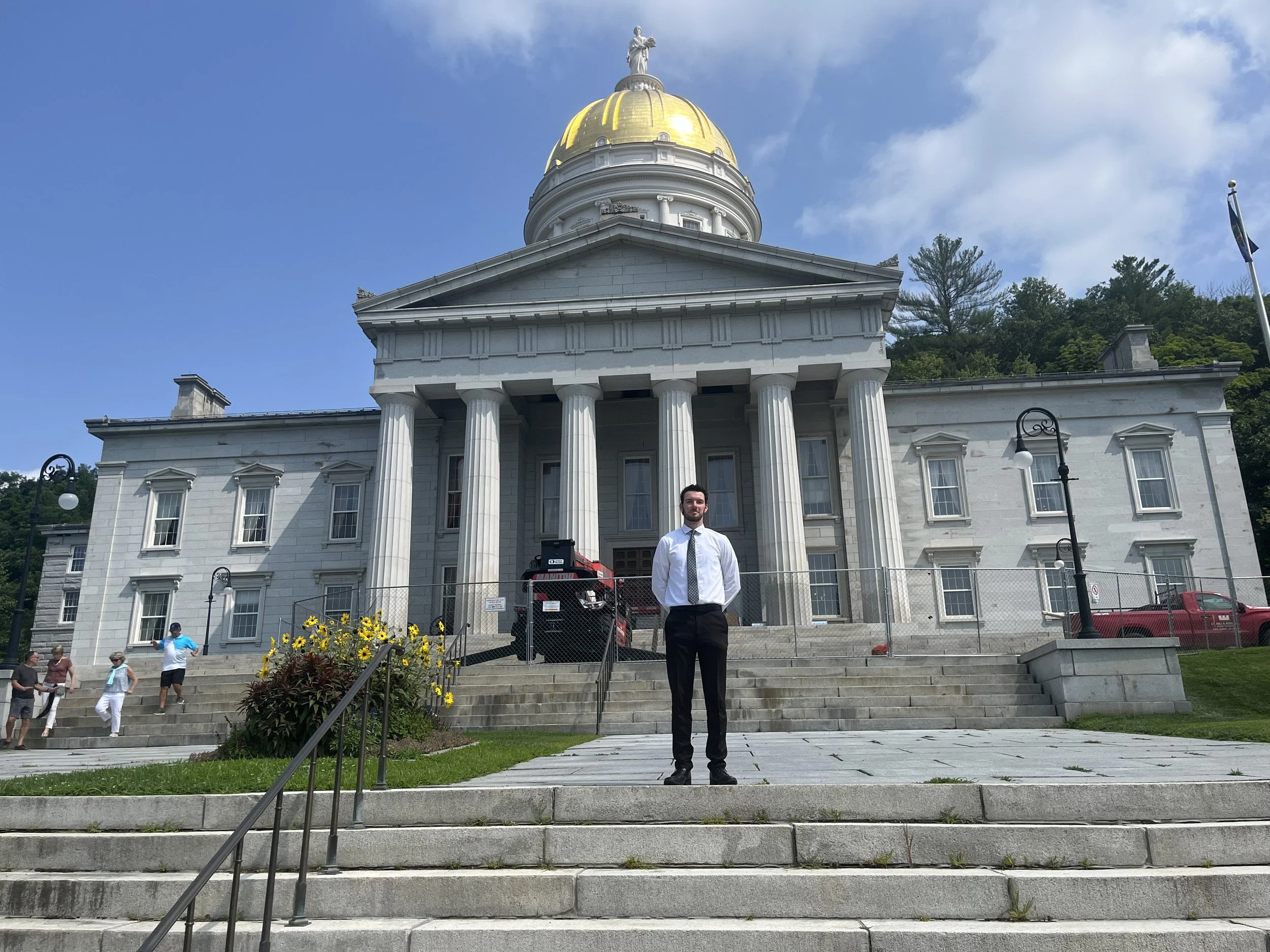 A man in a white shirt and tie standing on steps in front of the Vermont statehouse in Montpelier.