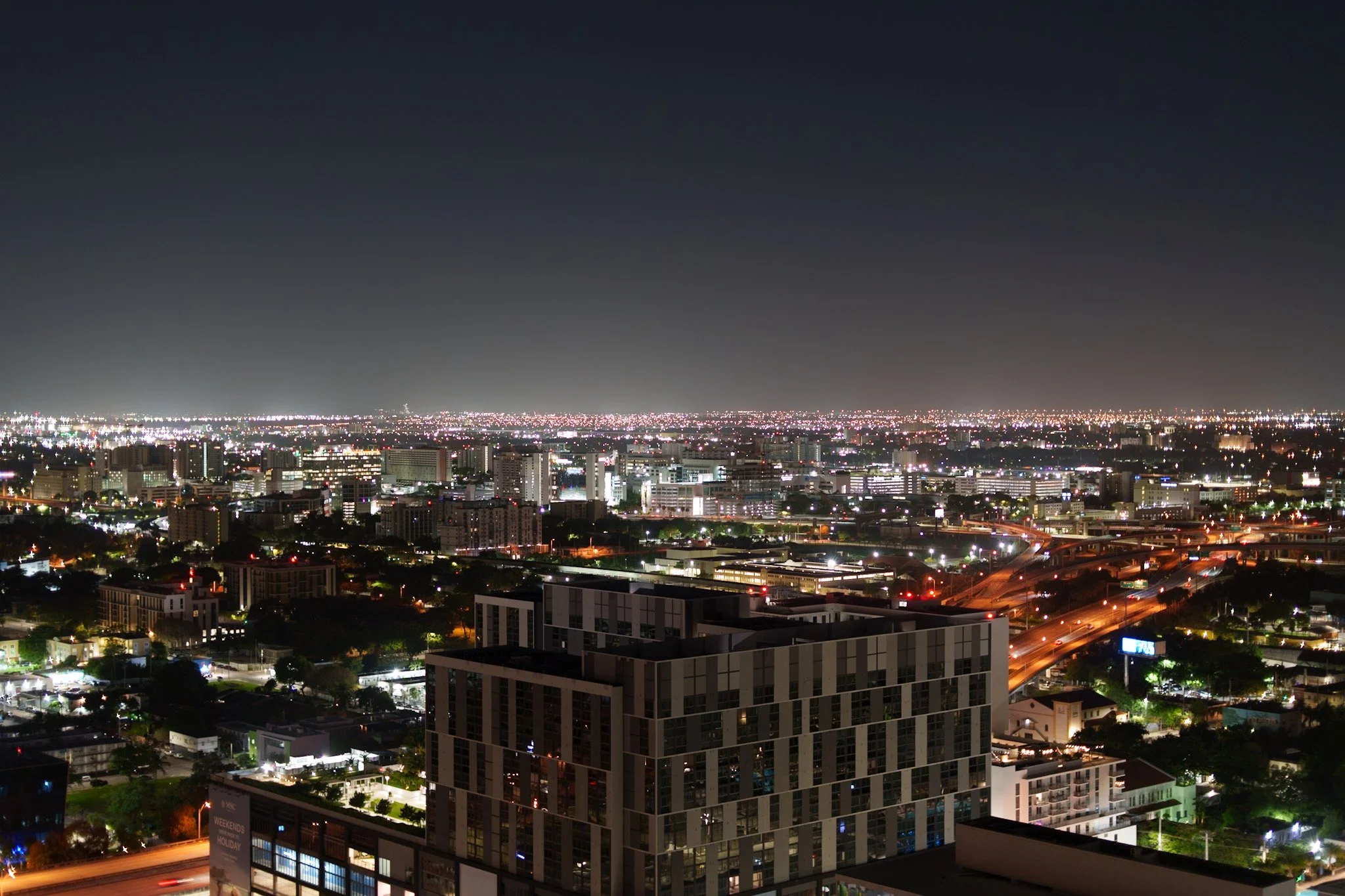 Nighttime cityscape with illuminated buildings, highways, and a dark sky.