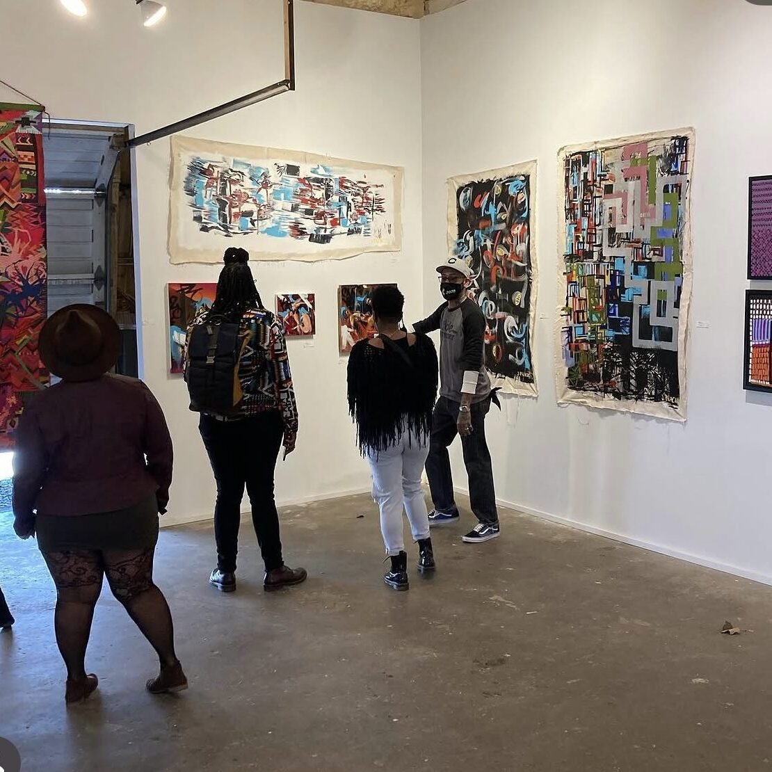 People viewing abstract paintings in an art gallery with white walls and concrete floor.