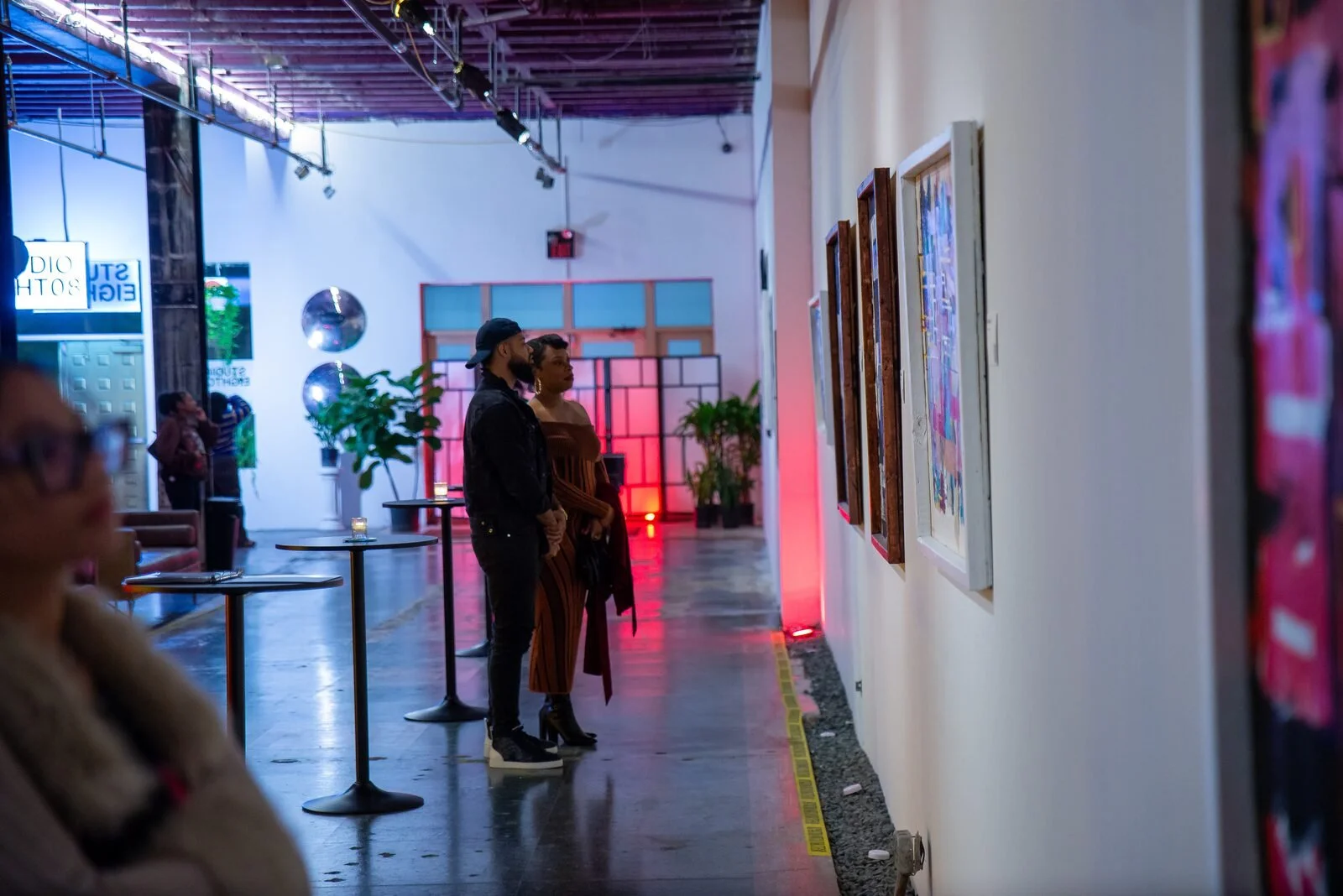 People viewing artwork in an art gallery with colorful lighting and decorative spheres.
