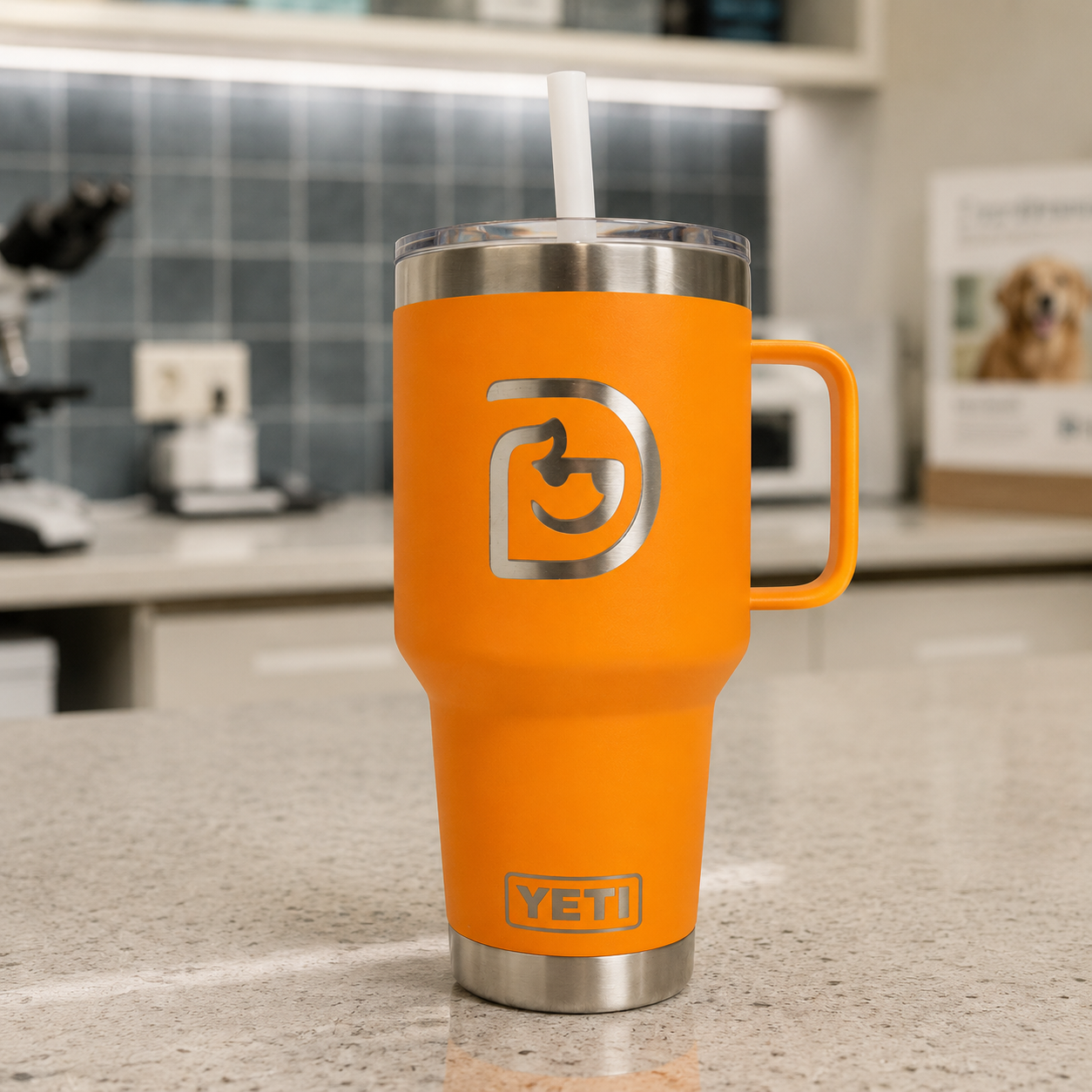Orange YETI tumbler with logo and stainless steel top and straw on a kitchen countertop.