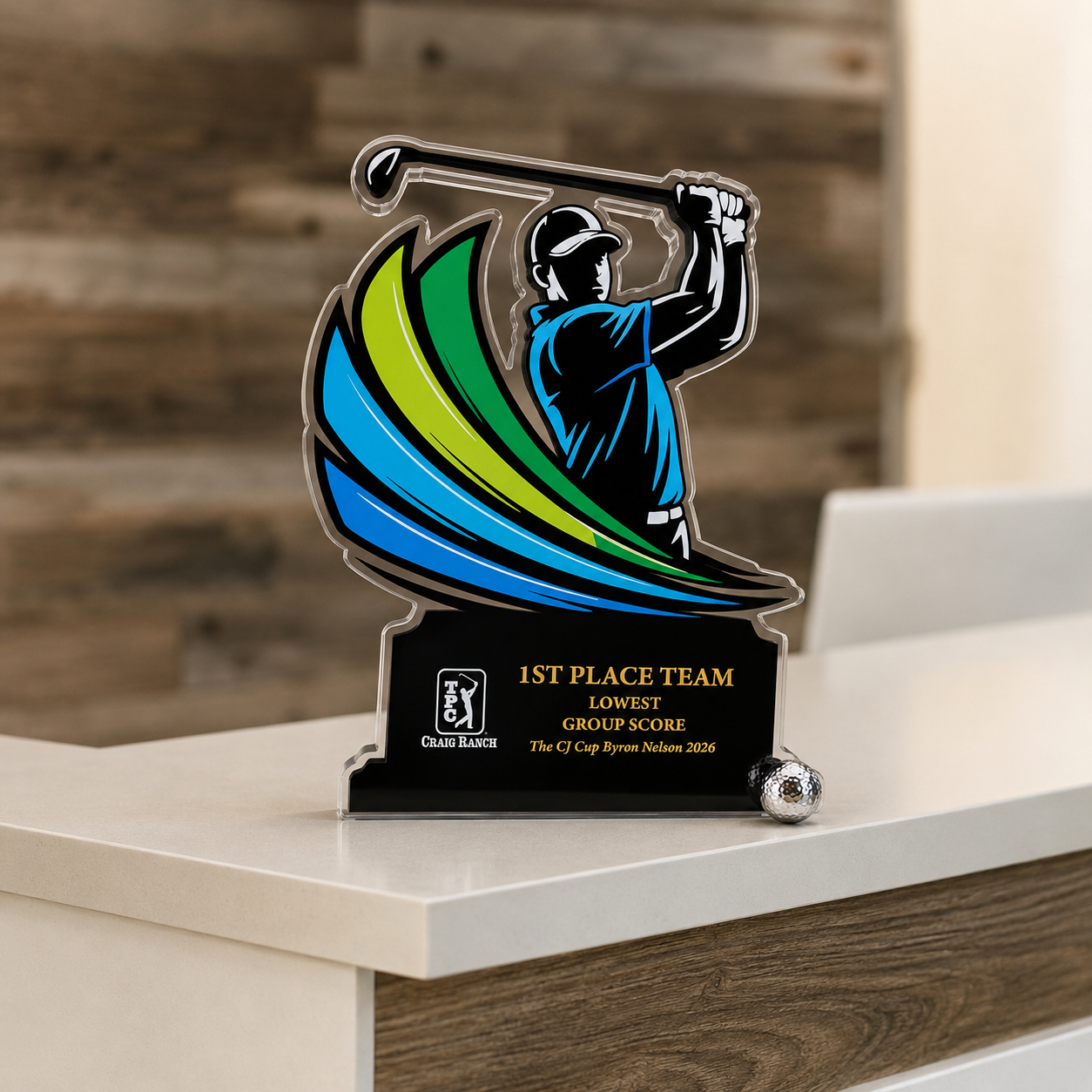 A trophy with a graphic of a golfer swinging a club, colored in blue, green, and black, with a golf ball at the base. The trophy is for the 1st place team with the lowest group score at the CJ Cup Byron Nelson 2026, awarded by Craig Ranch.