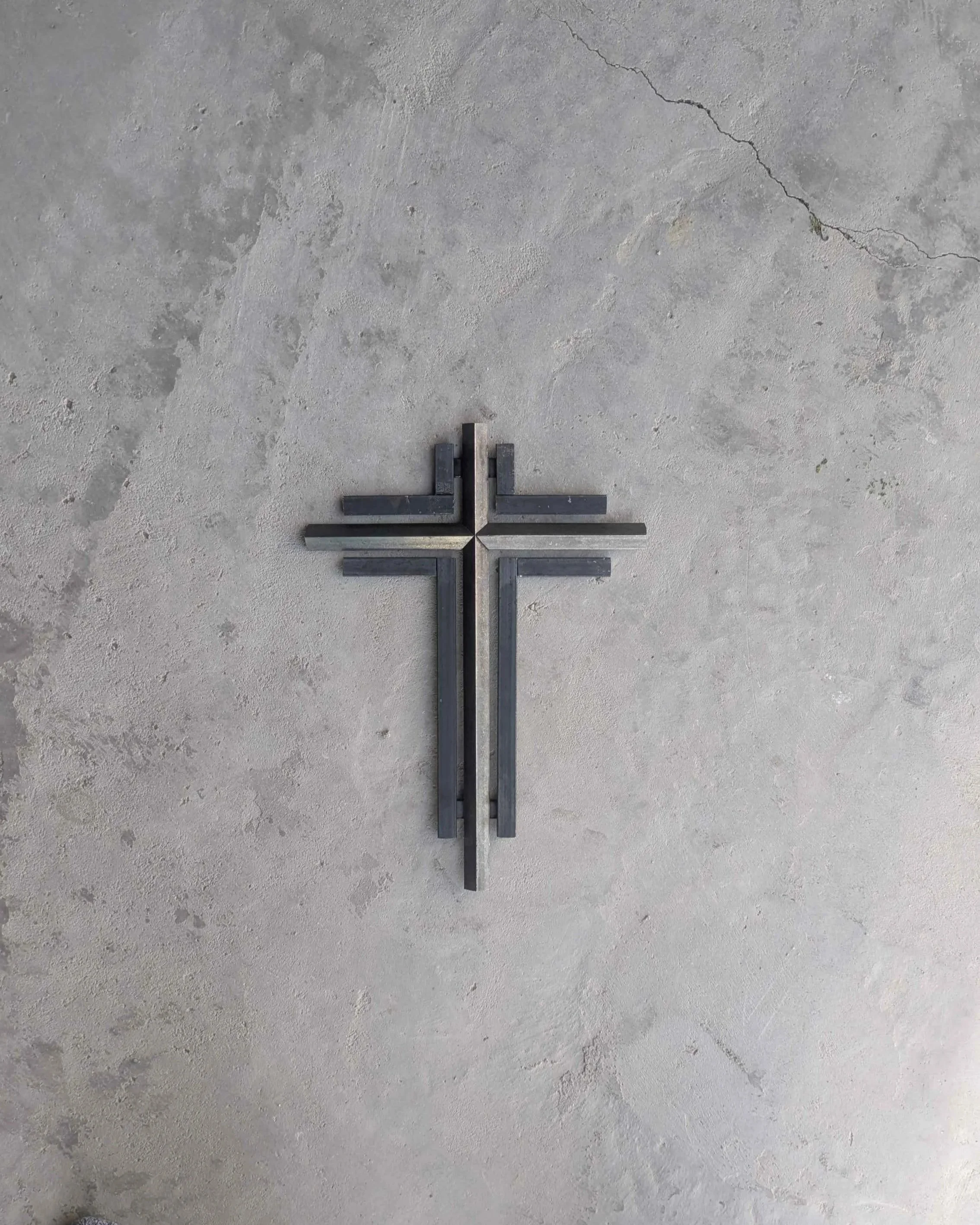 A metal art cross sculpture sitting on a concrete slab, intended for hanging on a wall as home decor.